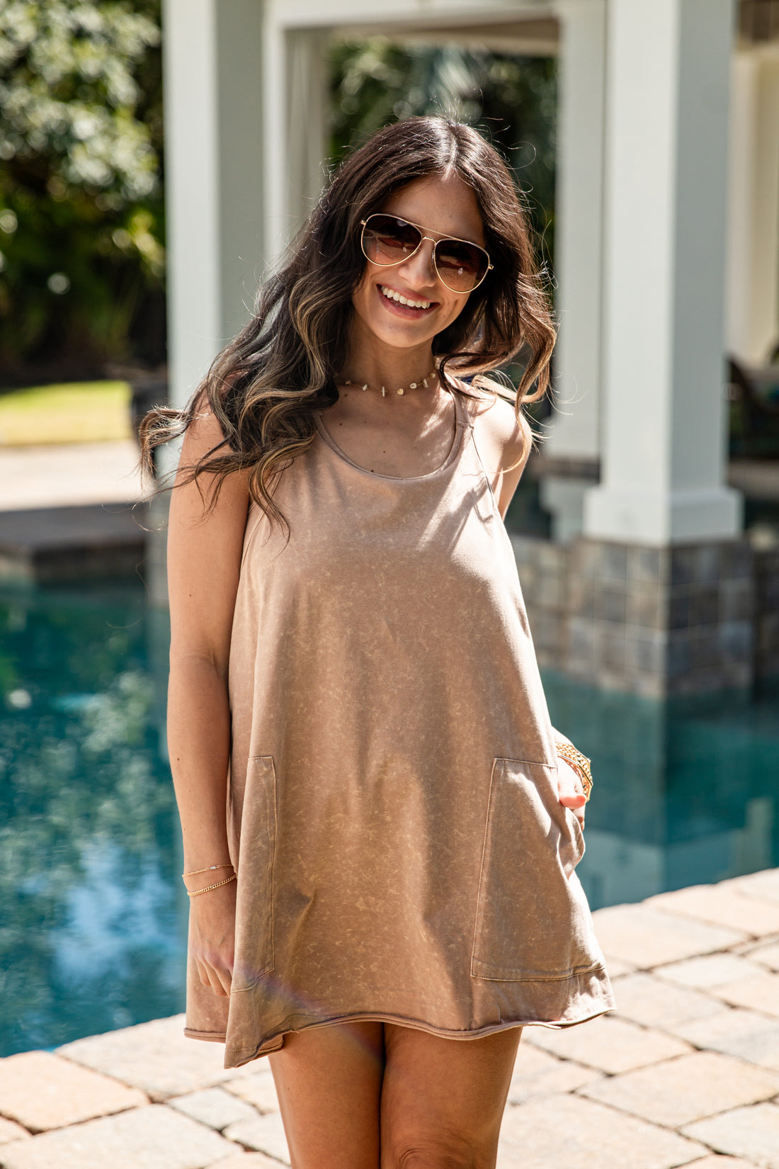 Woman wearing a beige dress and sunglasses by a pool