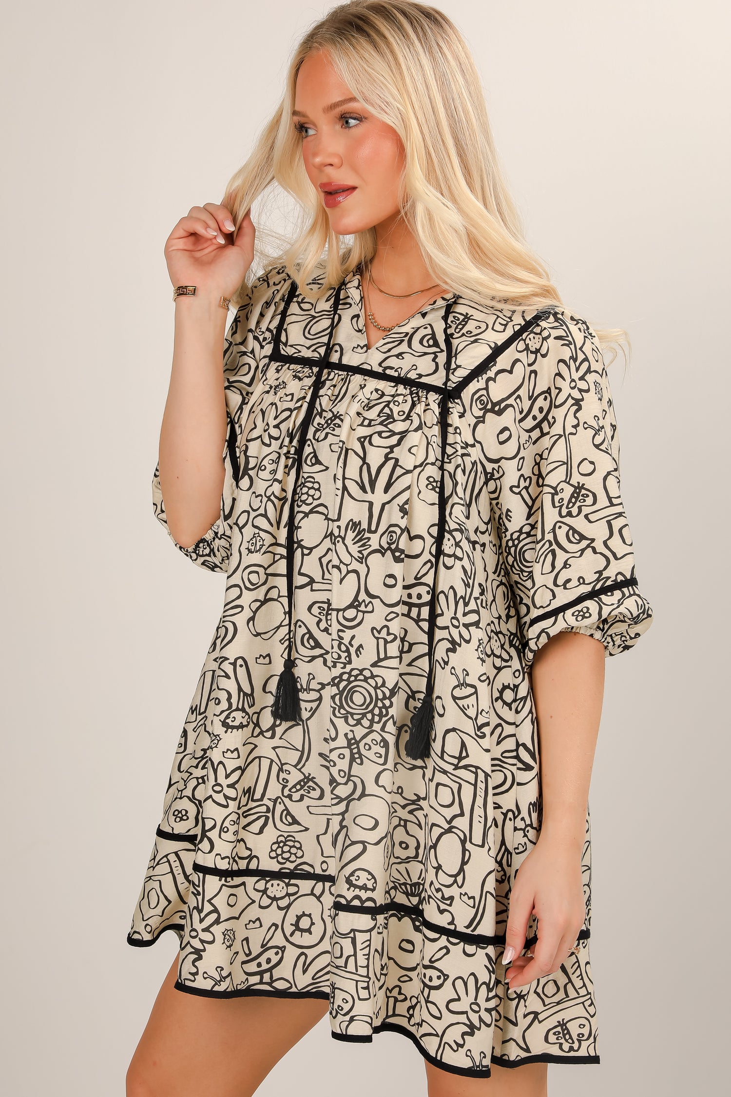 Woman wearing a black and white patterned dress with tassels on a plain background