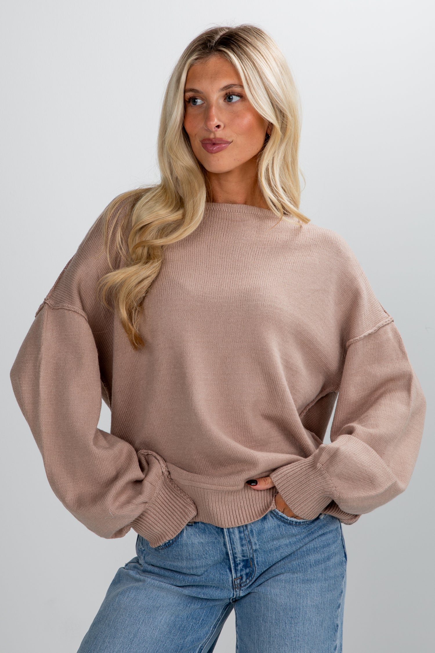 Woman wearing a beige sweater and blue jeans against a plain background