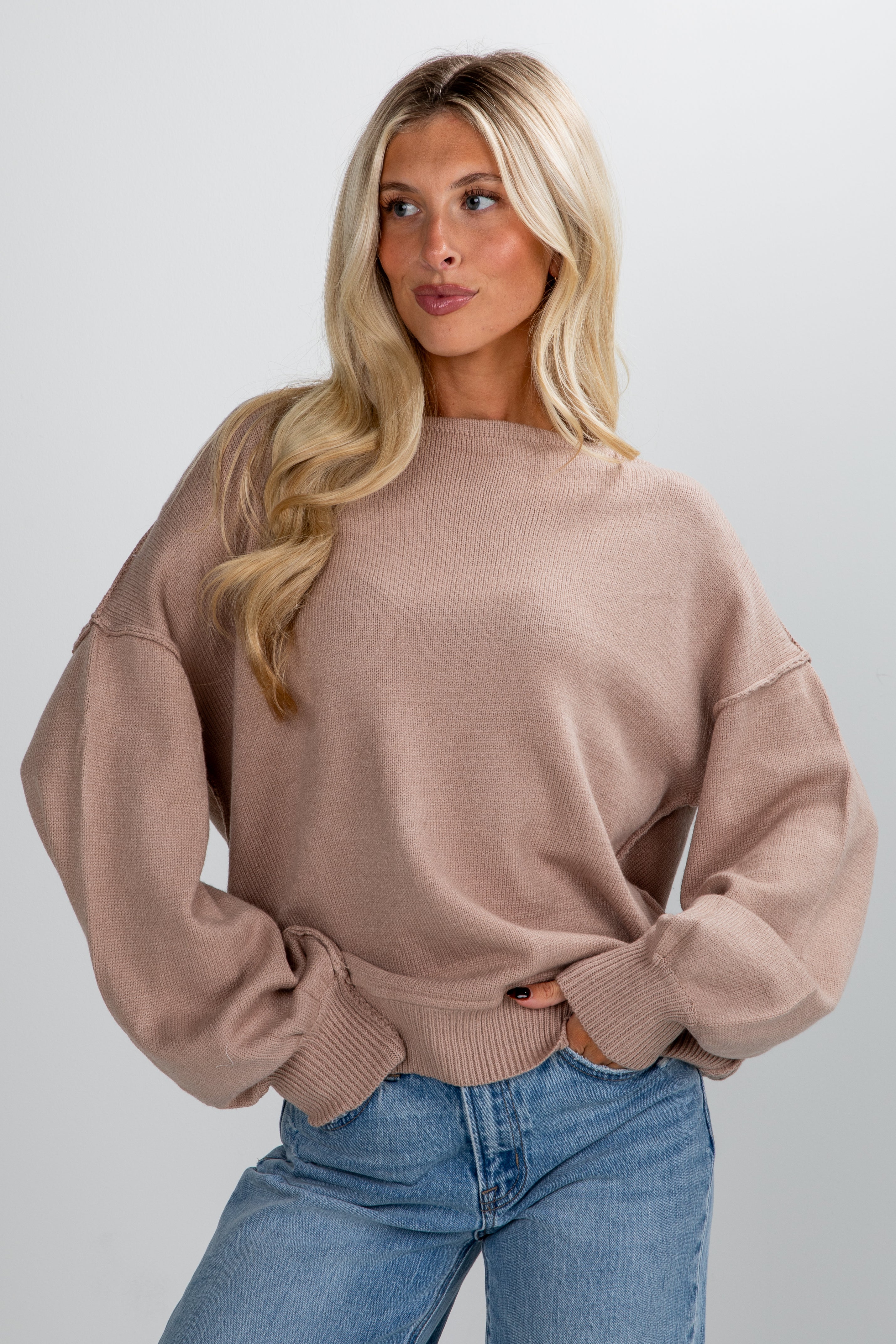 Woman wearing a beige sweater and blue jeans against a plain background