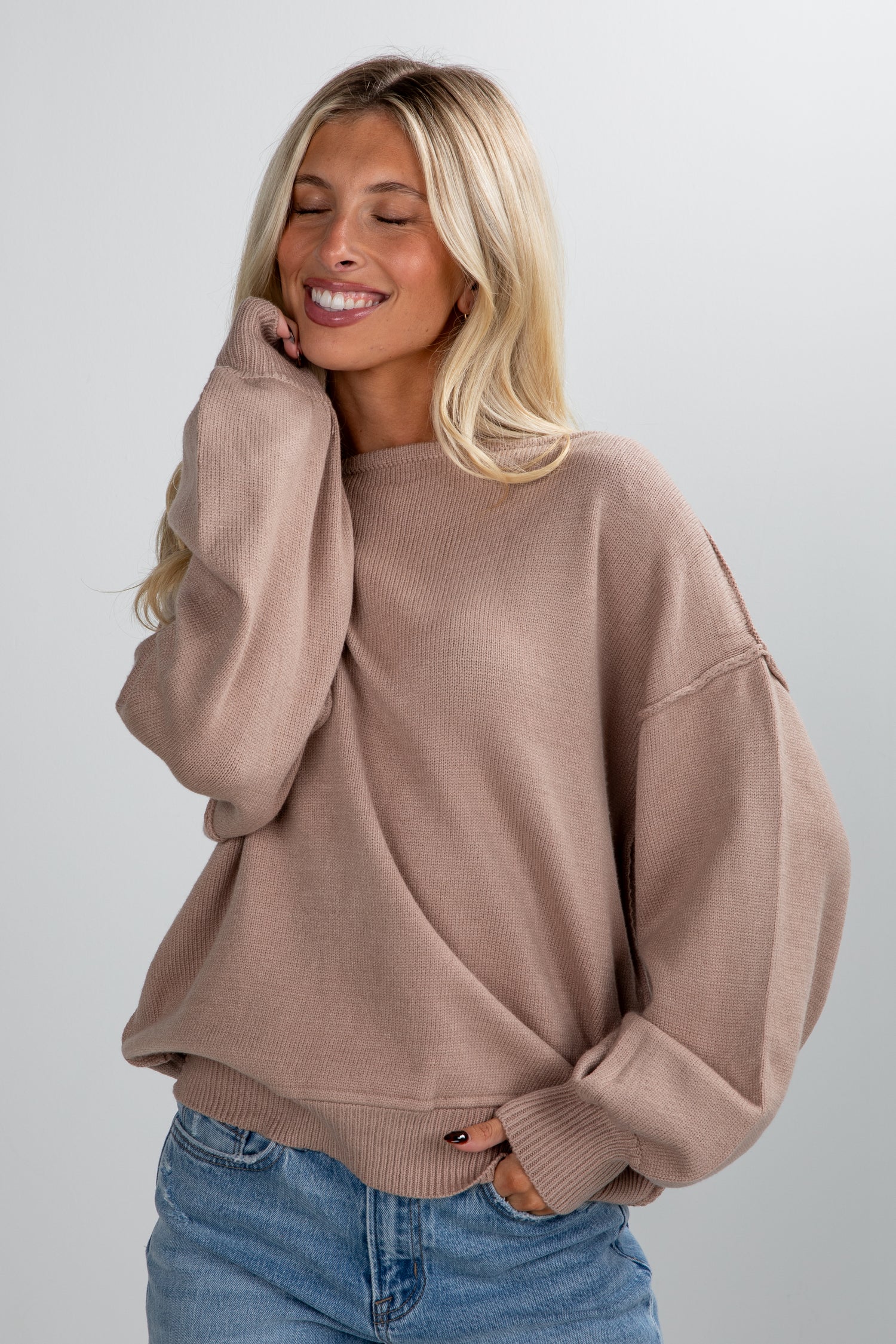 Woman wearing a brown sweater and blue jeans against a plain background