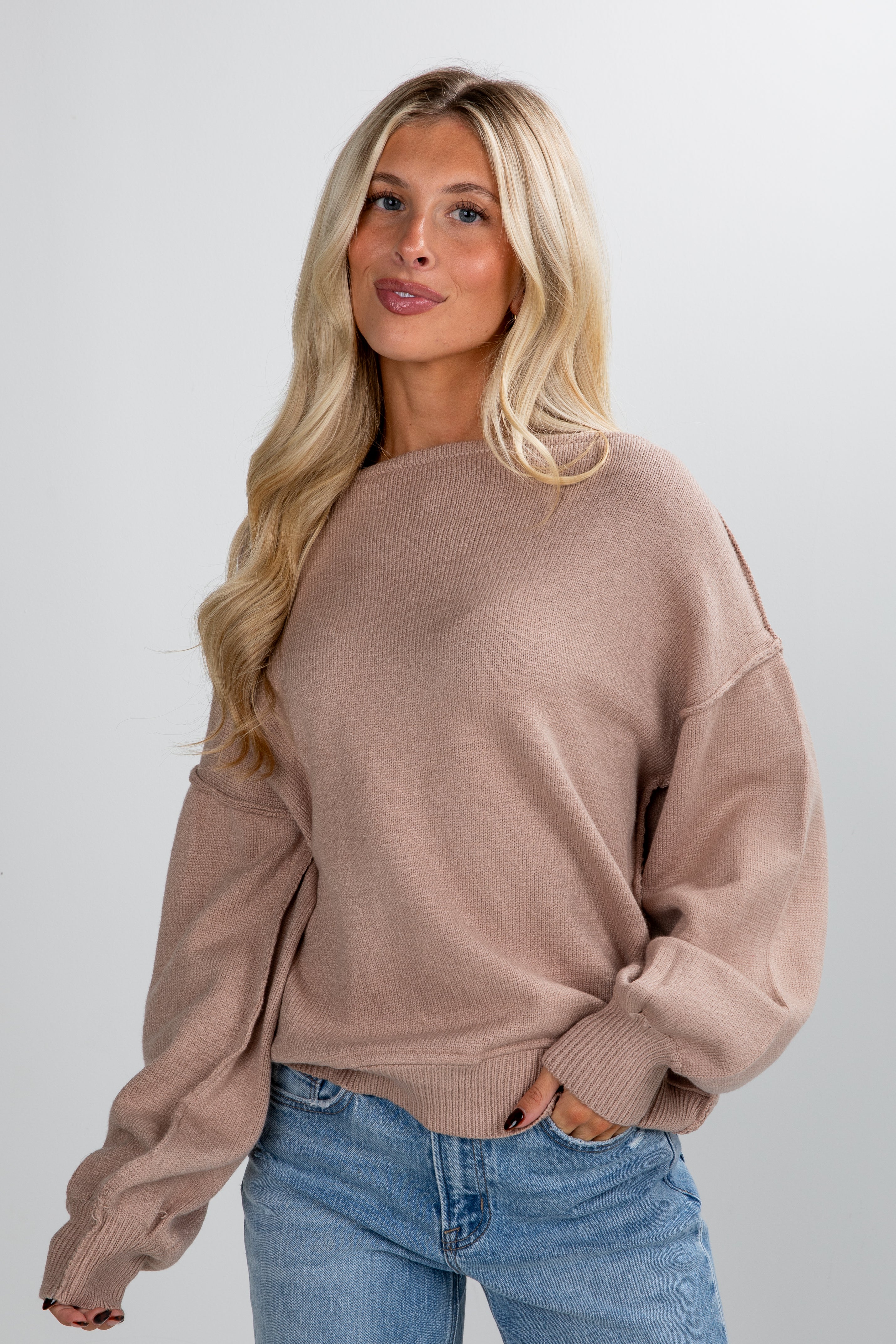 Woman wearing a beige sweater and blue jeans against a plain background
