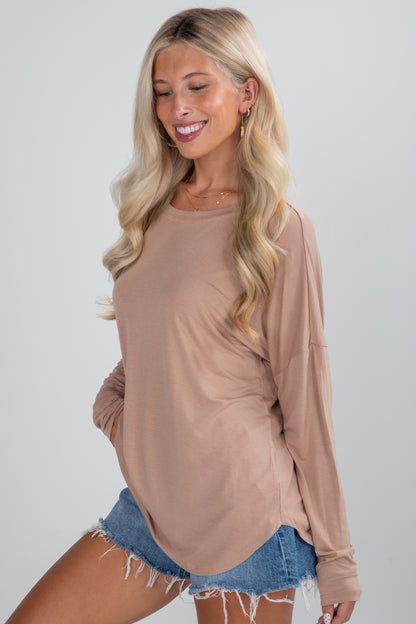 Woman wearing a beige long-sleeve top and denim shorts on a plain background