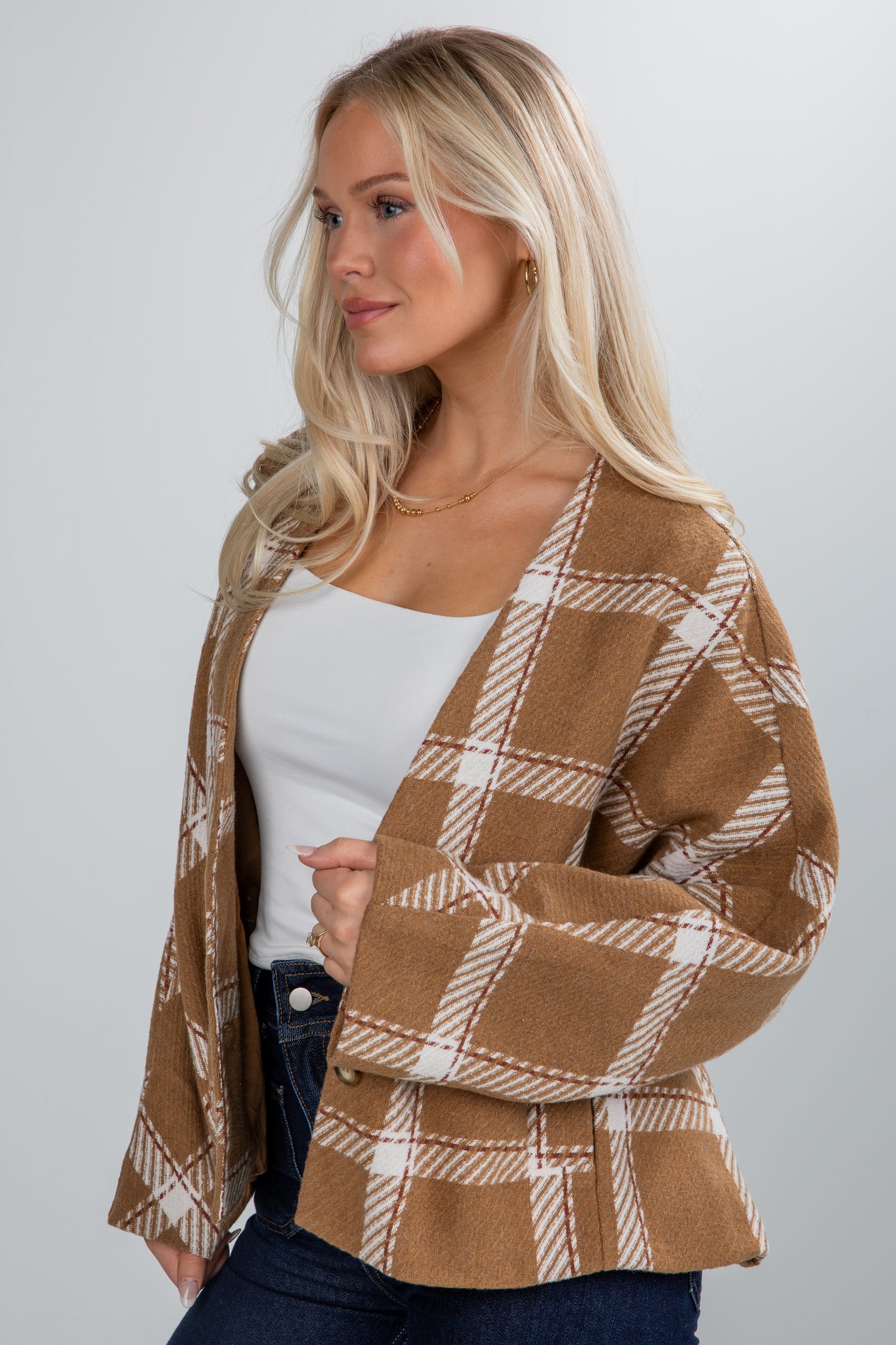 Woman wearing a brown and white plaid cardigan over a white top on a plain background