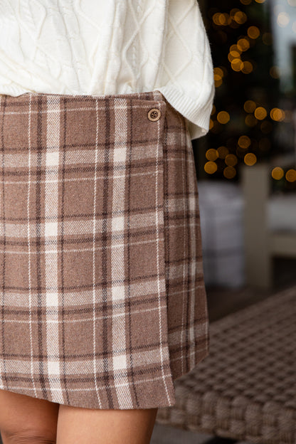 Brown plaid skirt worn with a white sweater against a blurred indoor background