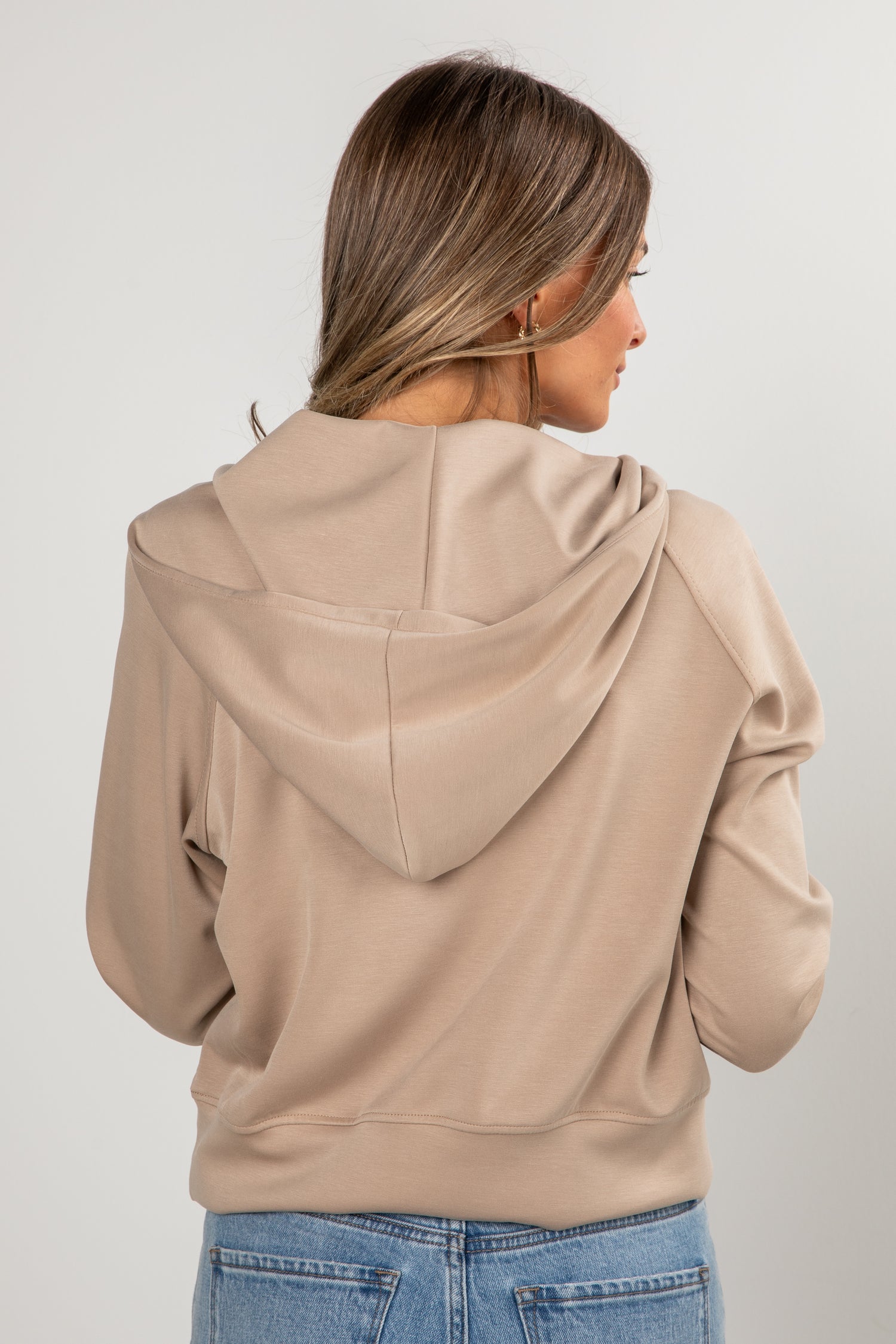 Woman wearing a beige hoodie from behind on a plain background