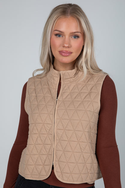 Woman wearing a beige quilted vest against a plain background