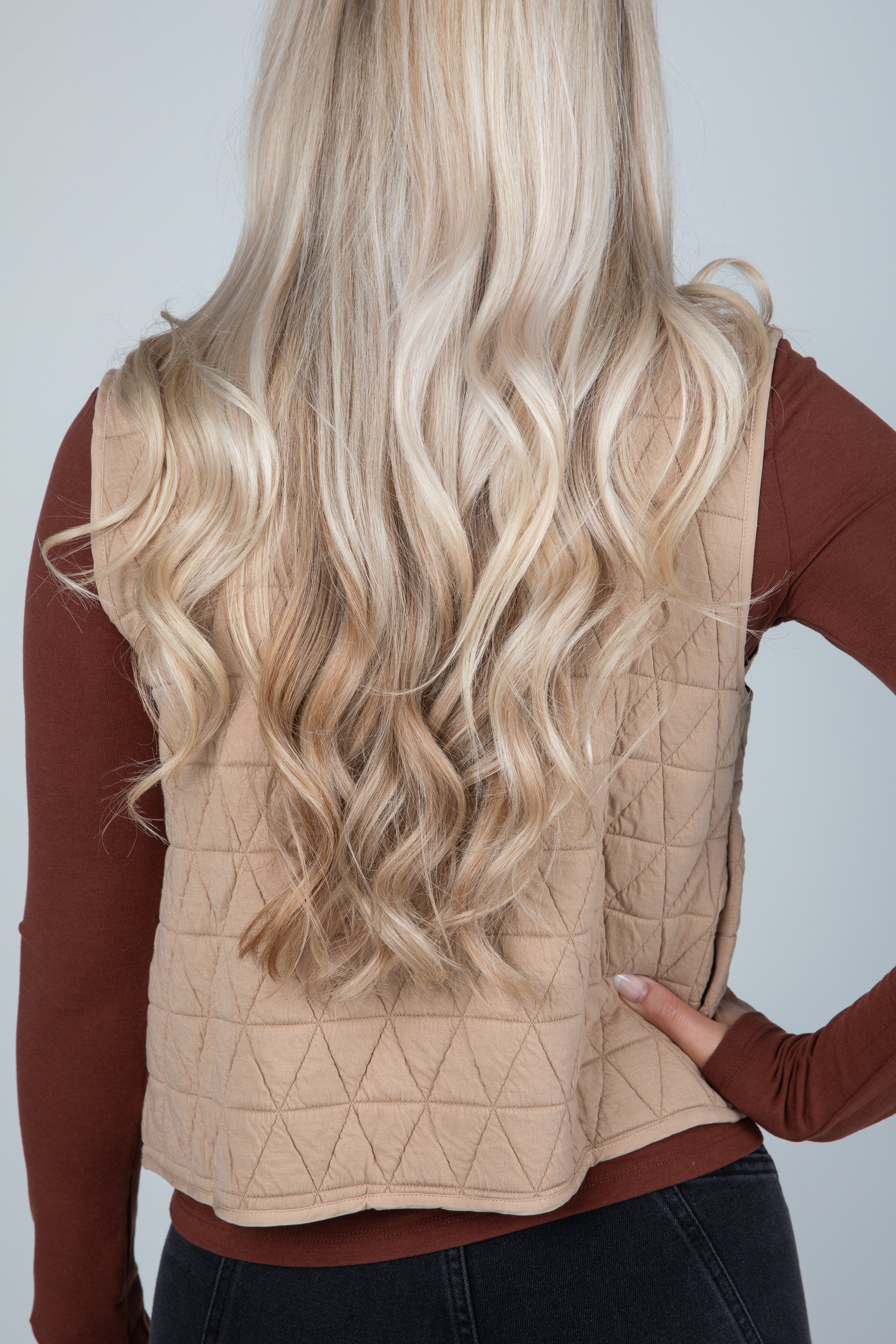 Person wearing a beige quilted vest with long blonde hair