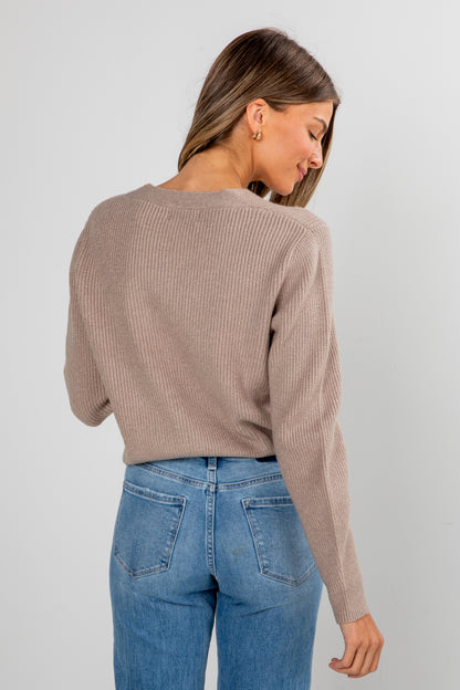 Woman wearing a beige ribbed sweater and blue jeans on a plain background