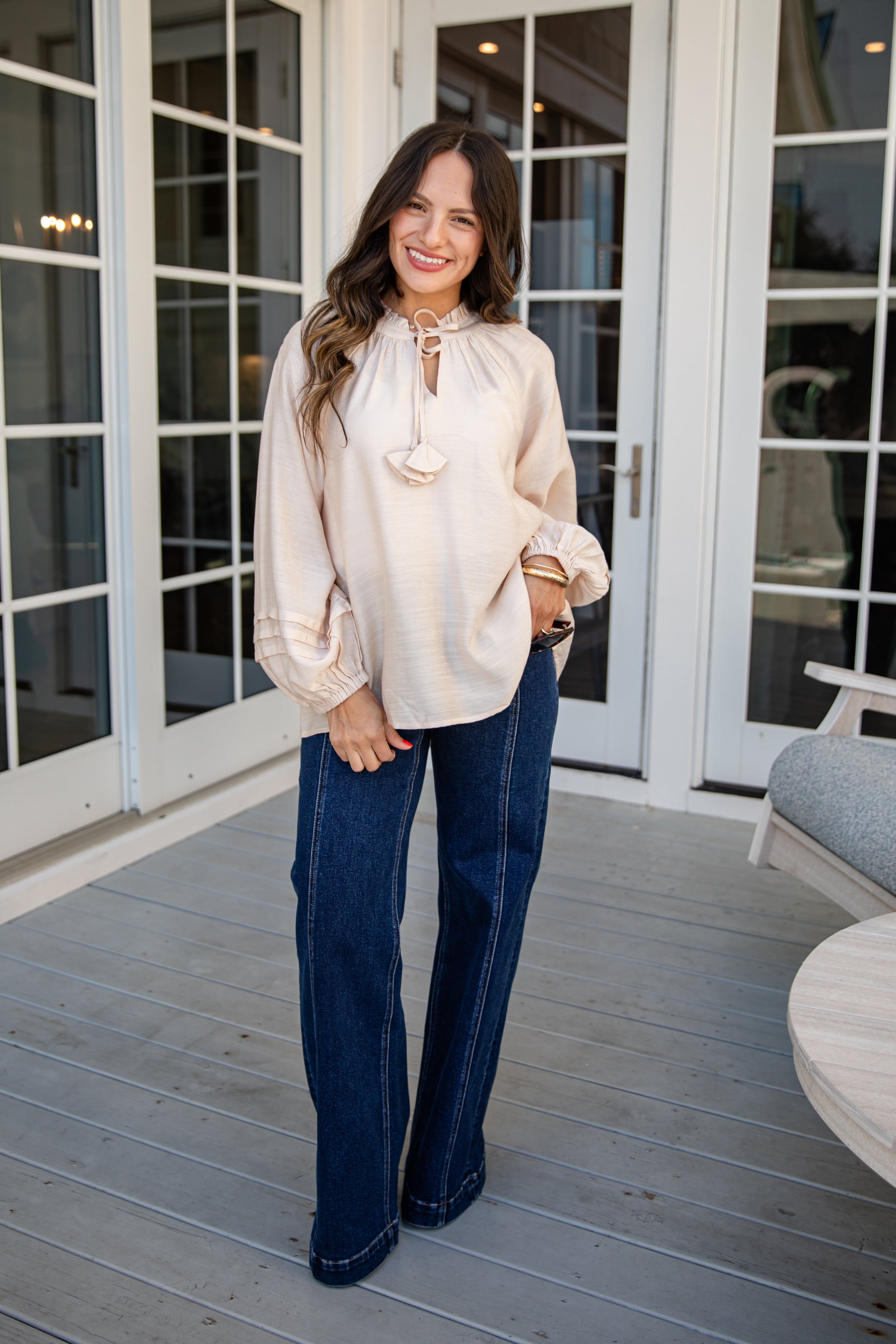 Woman wearing a white blouse and blue jeans standing on a wooden deck.