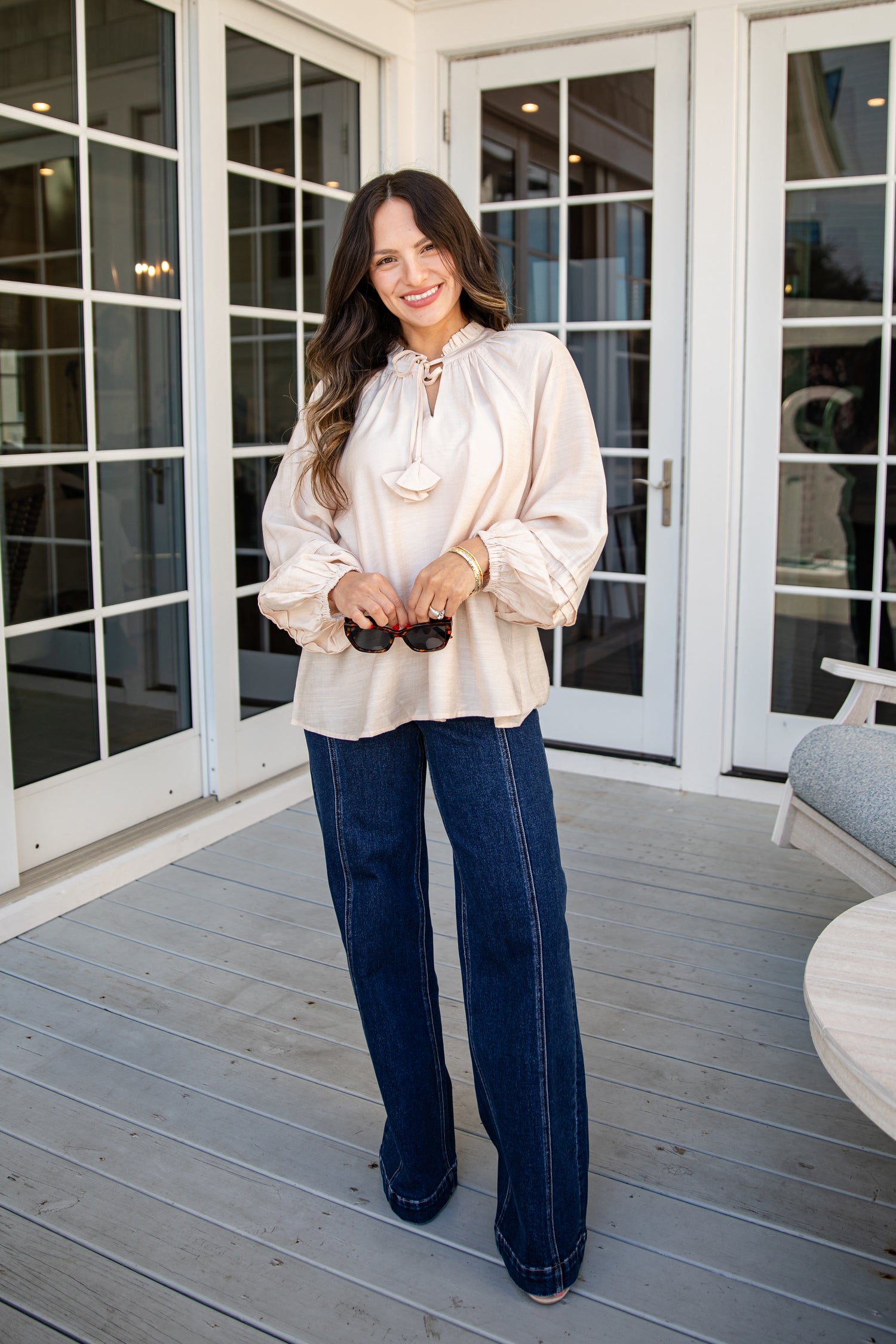 Woman in a white blouse and blue jeans standing on a wooden deck.