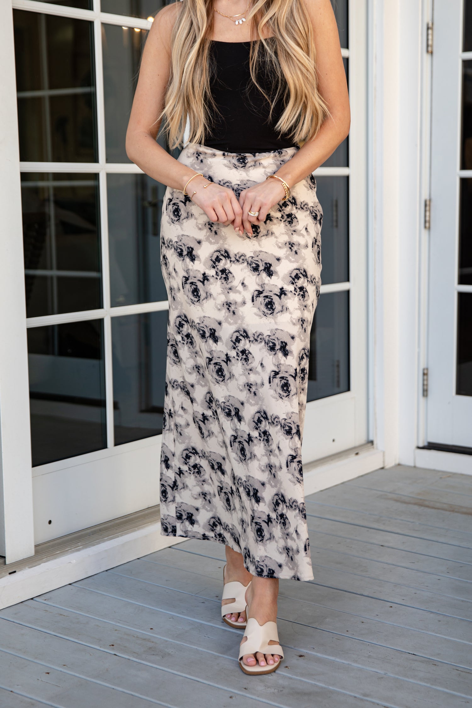 Woman wearing a black top and floral skirt on a wooden deck.