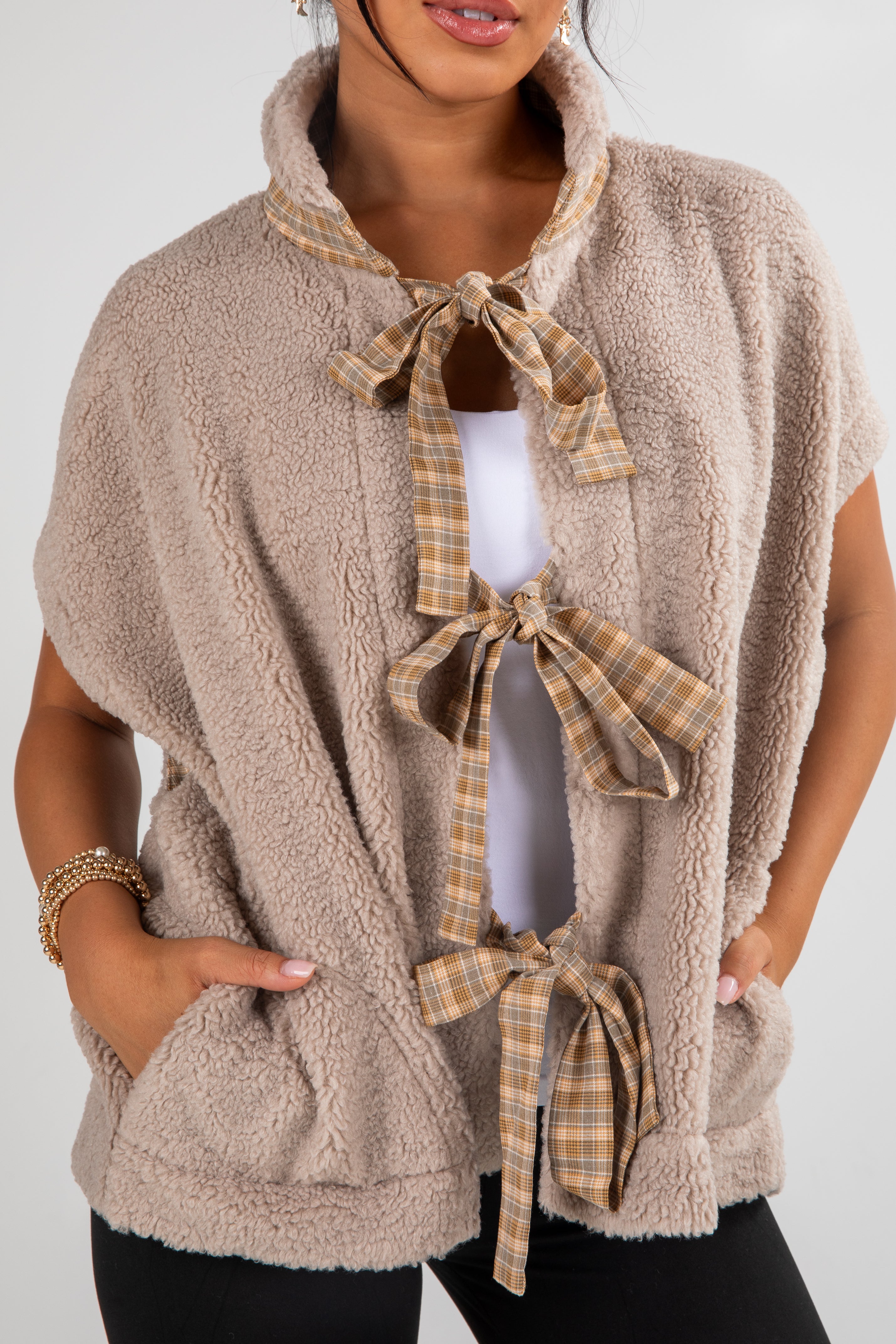 Beige fleece vest with plaid tie details worn by a person on a white background