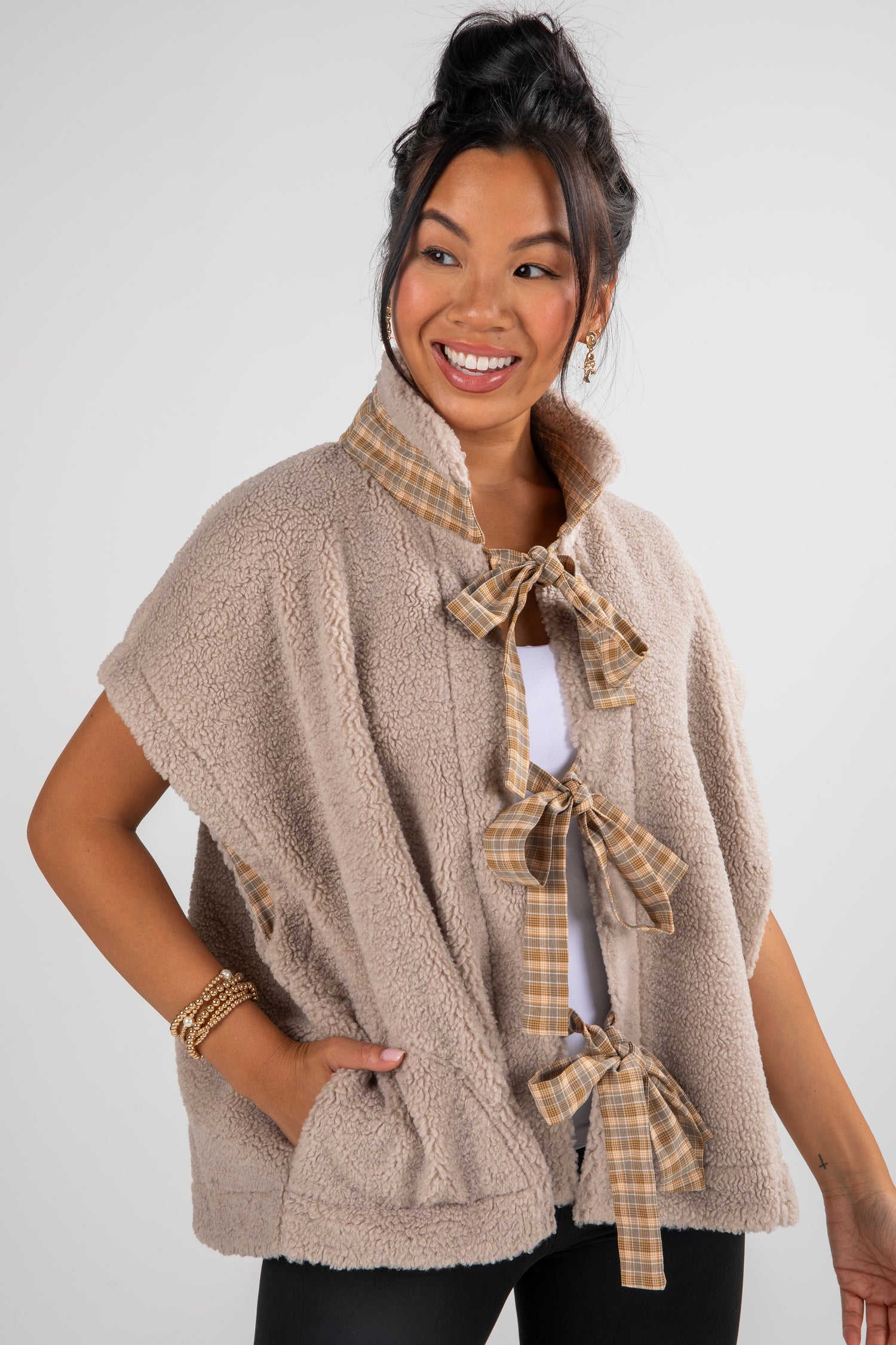 Woman wearing a beige fleece vest with plaid accents on a white background