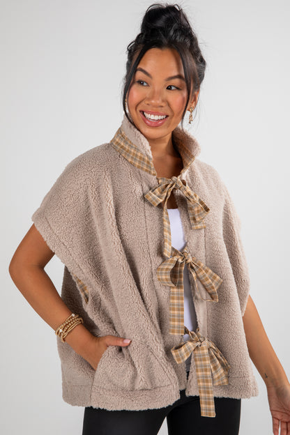 Woman wearing a beige fleece vest with plaid accents on a white background