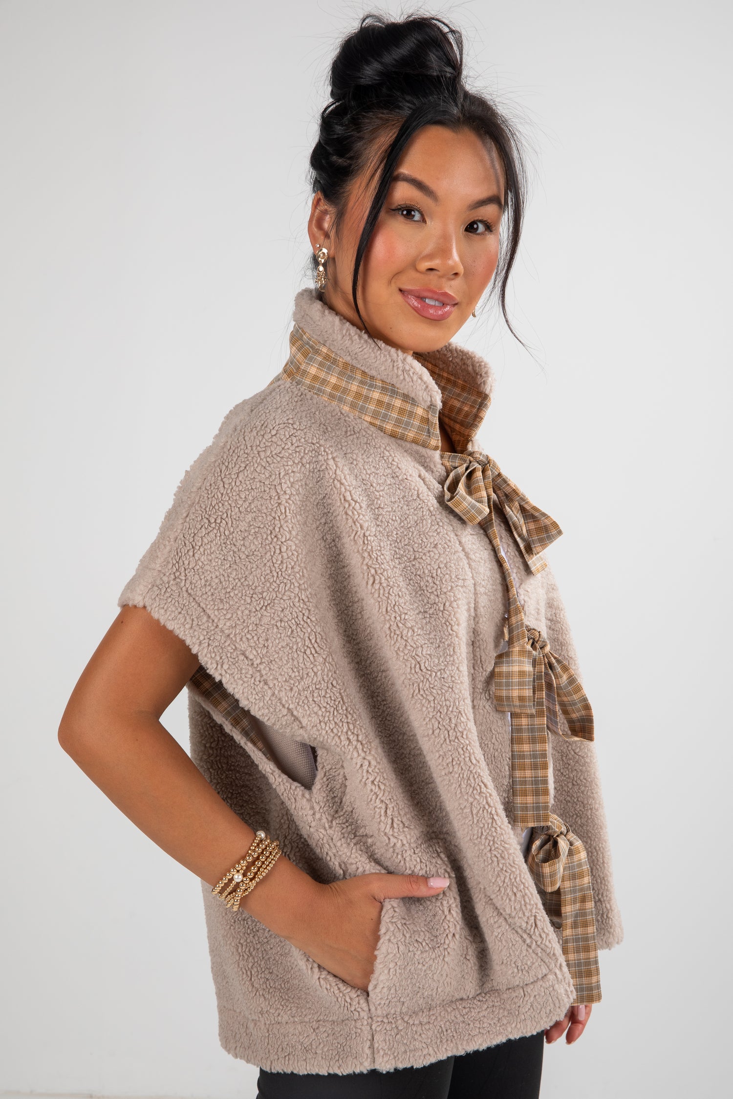 Woman wearing a beige fleece vest with plaid accents on a white background