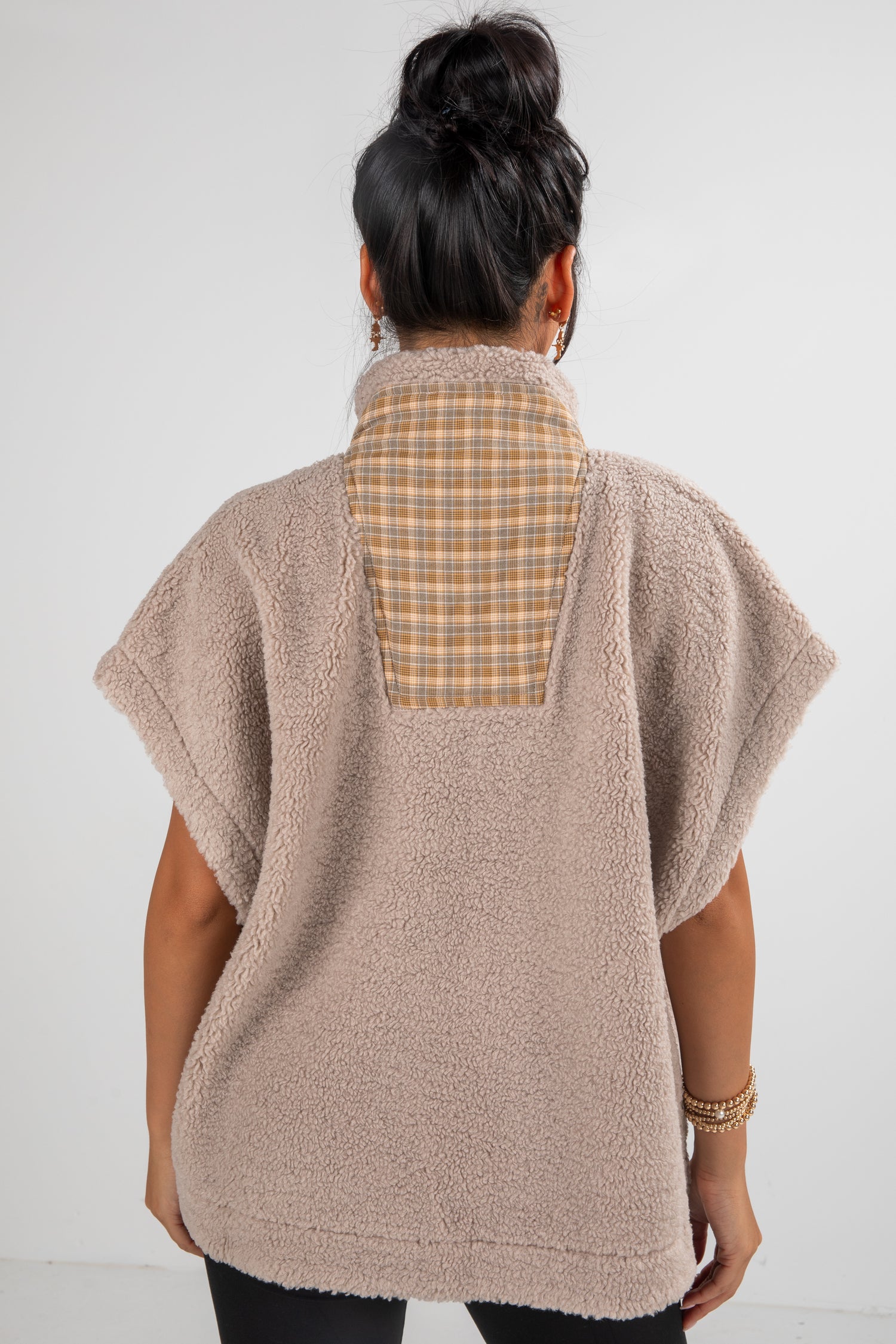 Person wearing a beige fleece poncho over a plaid shirt on a white background