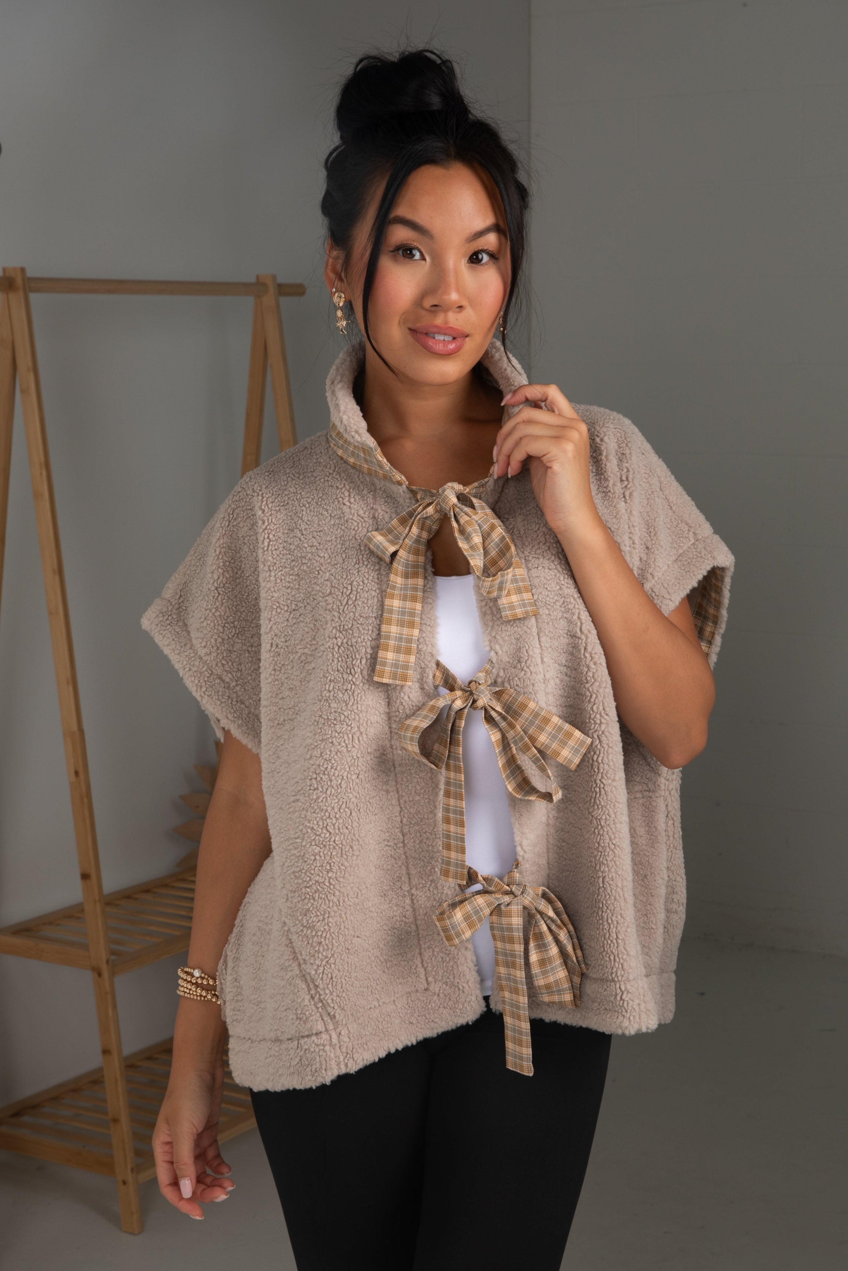 Woman wearing a beige knitted poncho with plaid accents in a minimalistic setting.