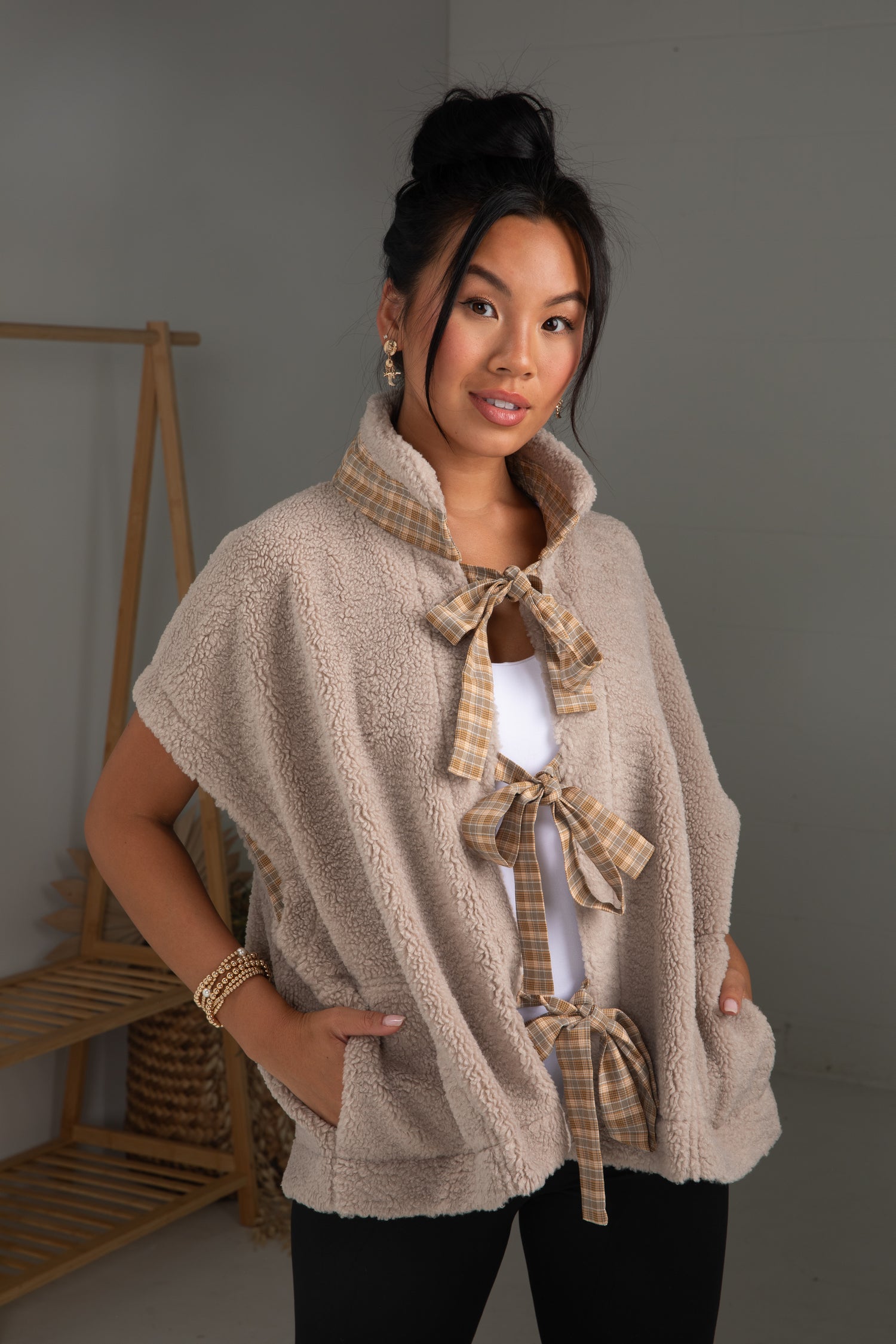 Woman wearing a beige cape with plaid accents in a neutral setting