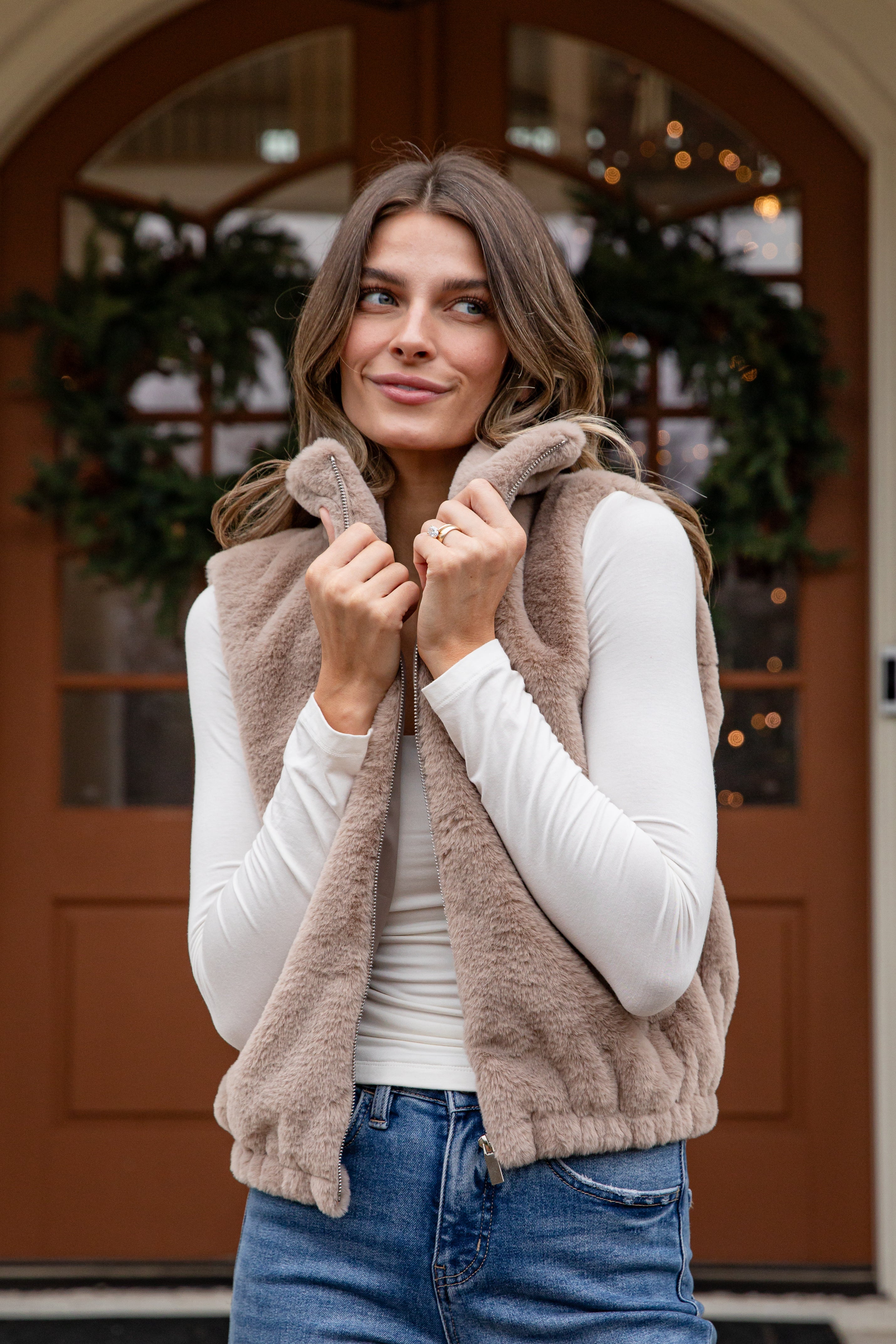 Woman wearing a brown fleece vest in front of a door with wreaths.