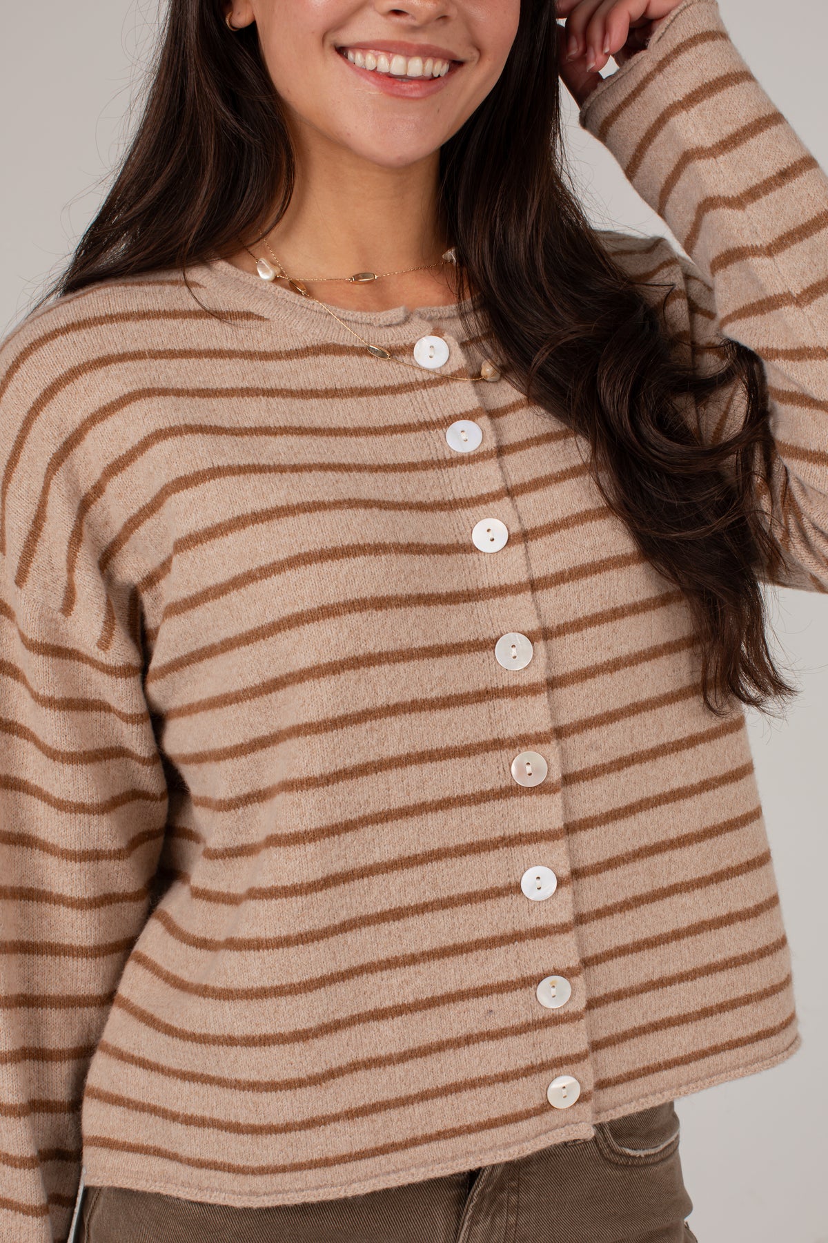A woman wearing a cropped, long-sleeve knit cardigan with horizontal brown stripes on a beige background, featuring a button-down front.