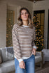 Woman wearing a striped sweater and jeans standing in a living room with a Christmas tree in the background.