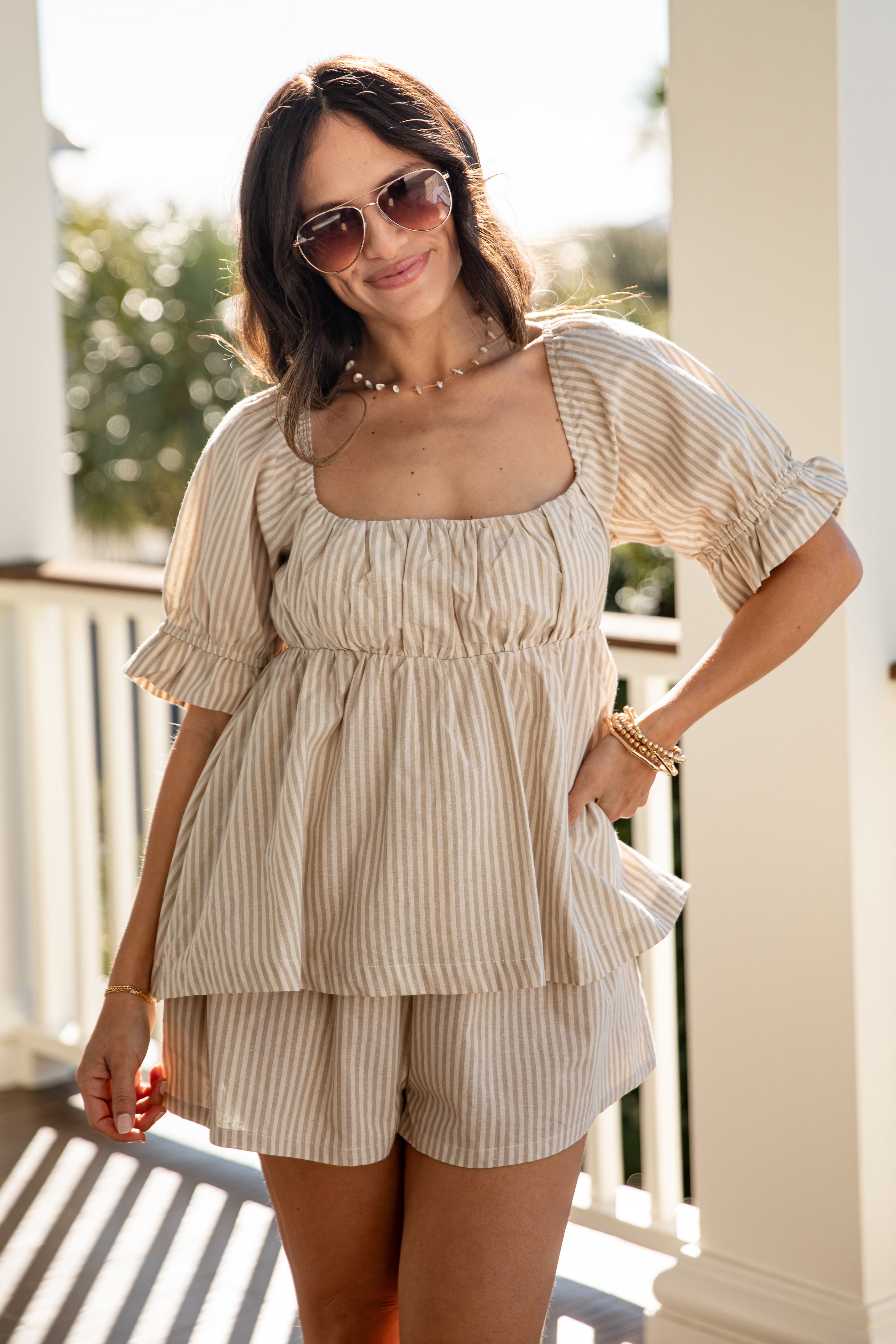 Woman wearing a beige striped outfit with sunglasses on a sunny day.