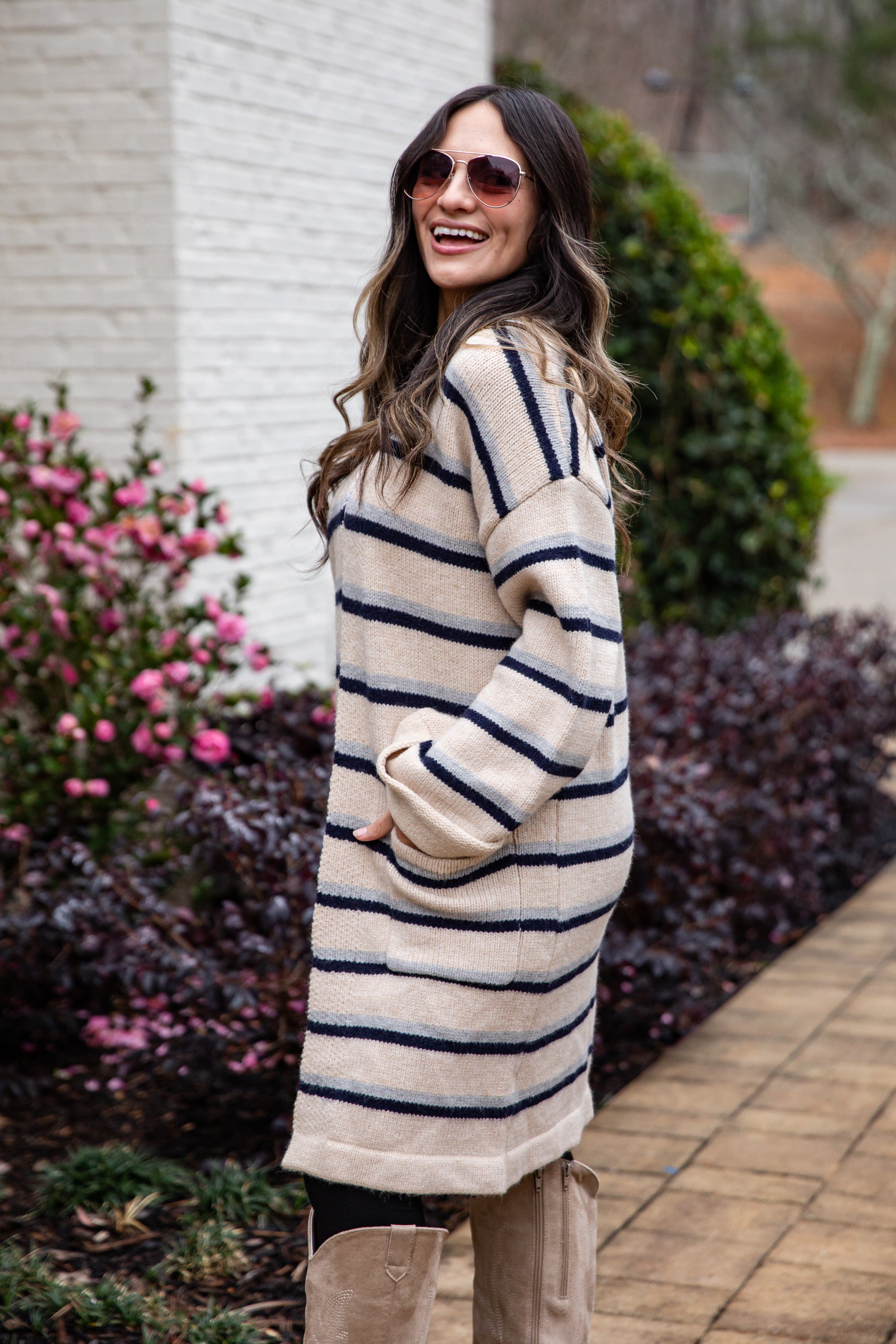 Woman wearing a striped sweater standing outdoors with plants and flowers in the background