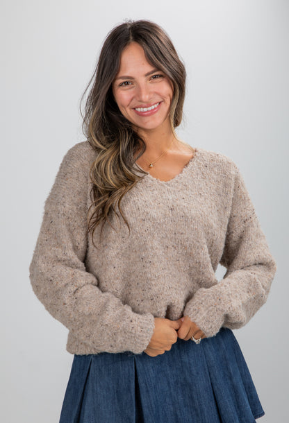 Woman wearing a beige sweater and blue skirt against a plain background