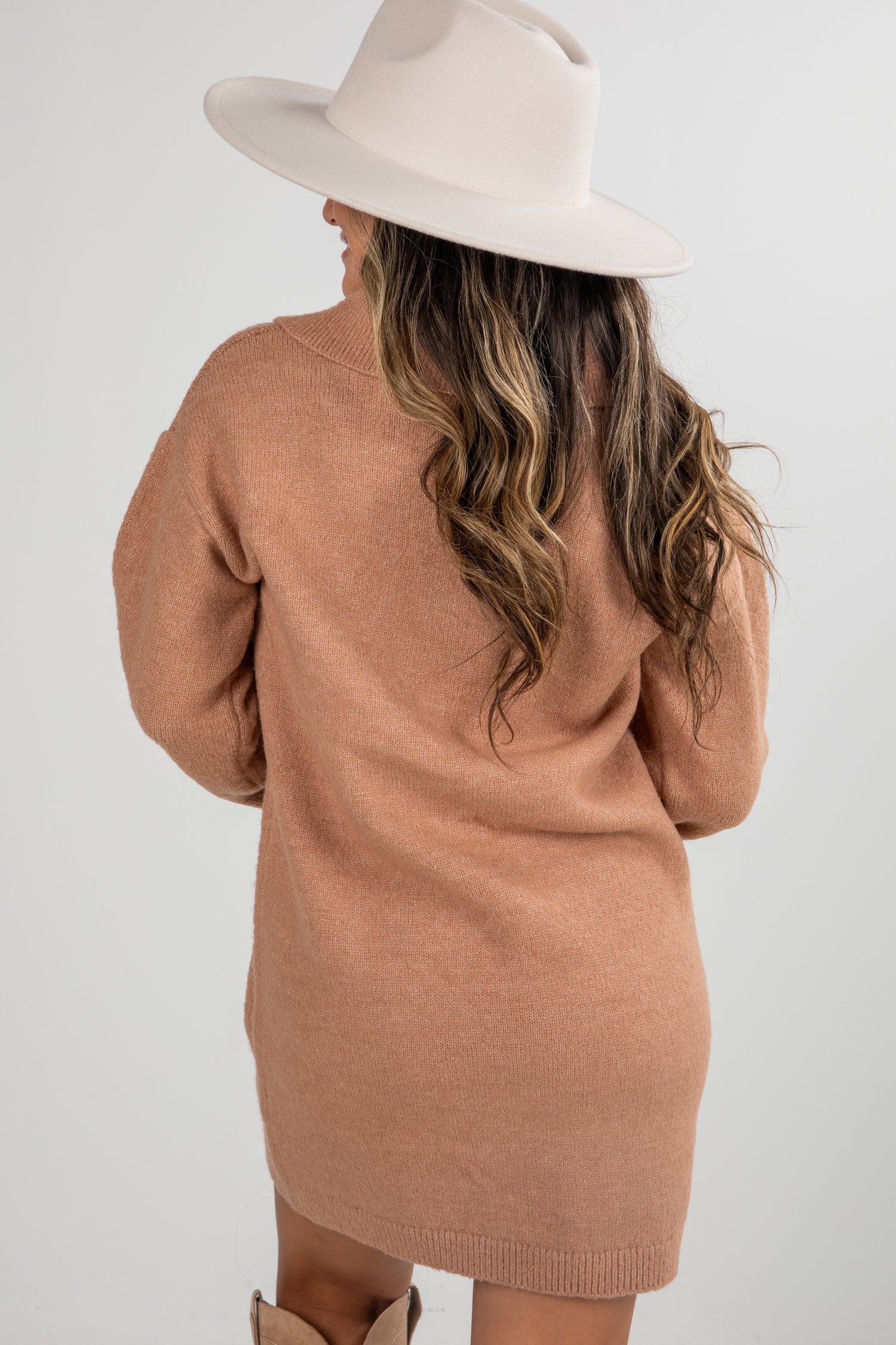 Woman wearing a brown sweater dress and beige hat on a white background
