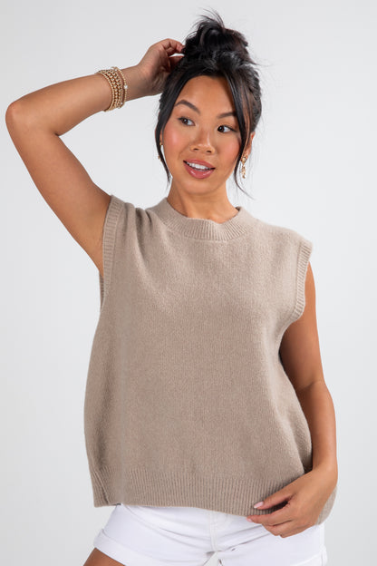 Woman wearing a beige sleeveless sweater against a white background
