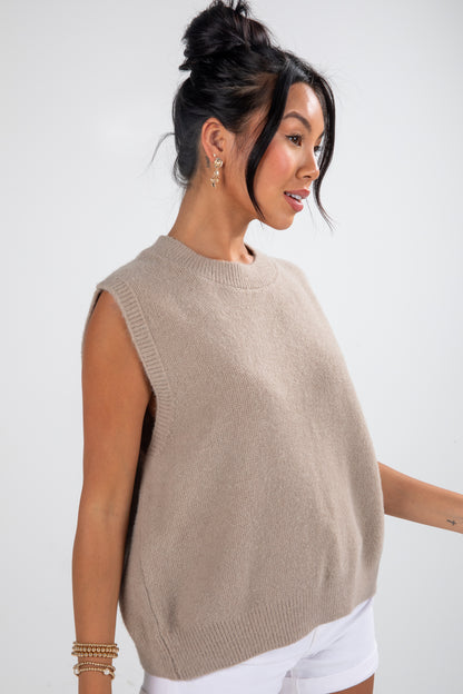 Woman wearing a beige sleeveless sweater against a white background