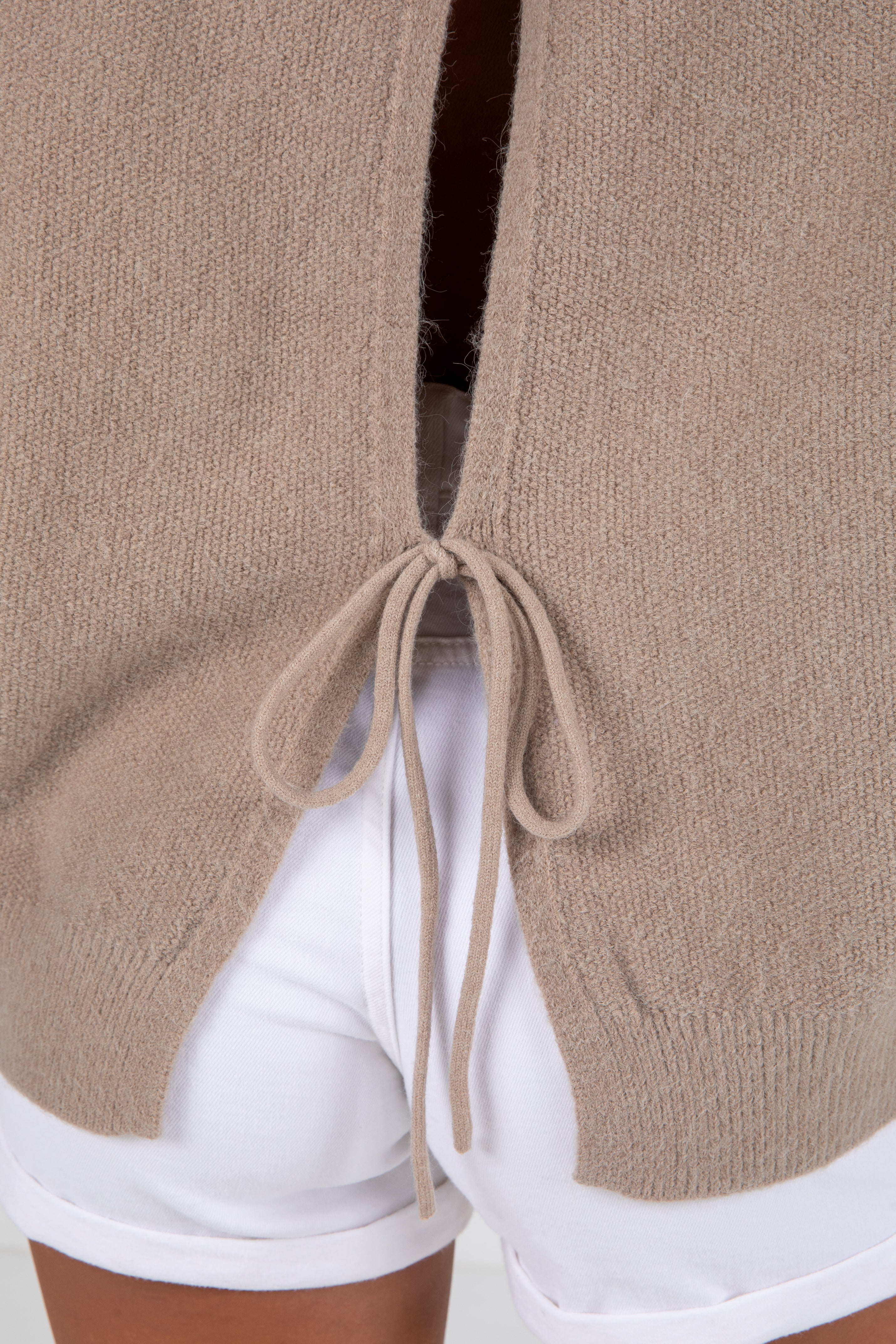 Close-up of a beige cardigan with drawstrings worn over white shorts.