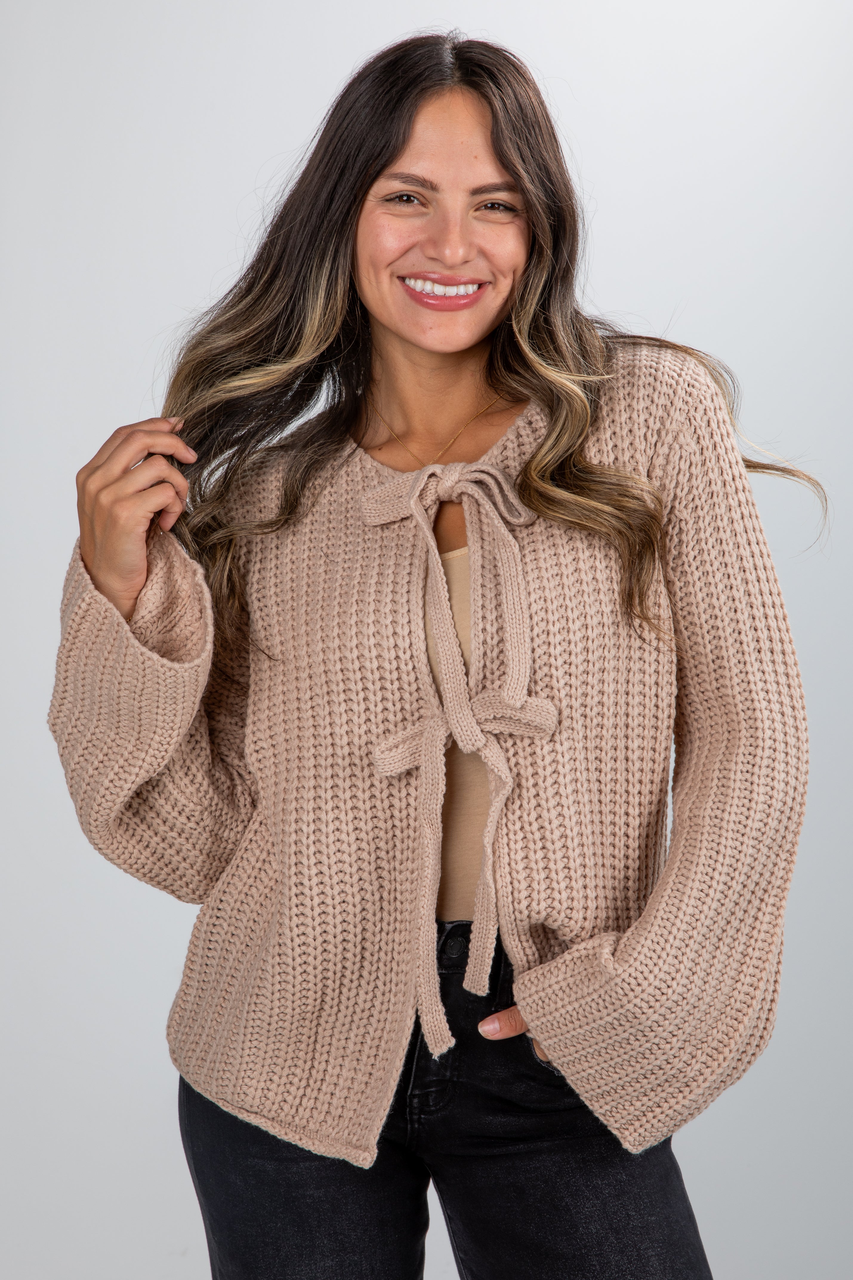 Woman wearing a beige knitted cardigan with a tie detail on a plain background