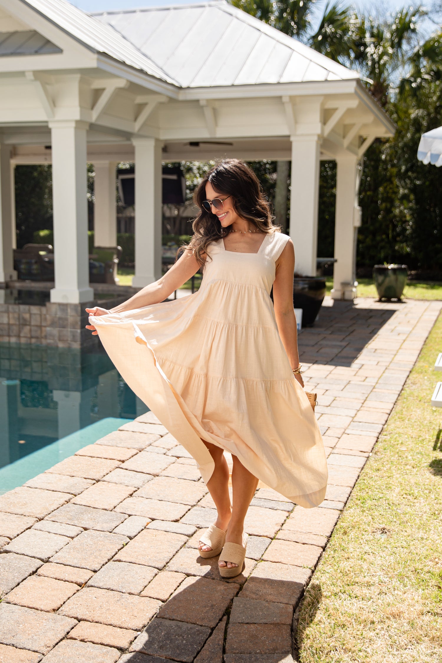 Woman in a beige dress standing by a poolside gazebo