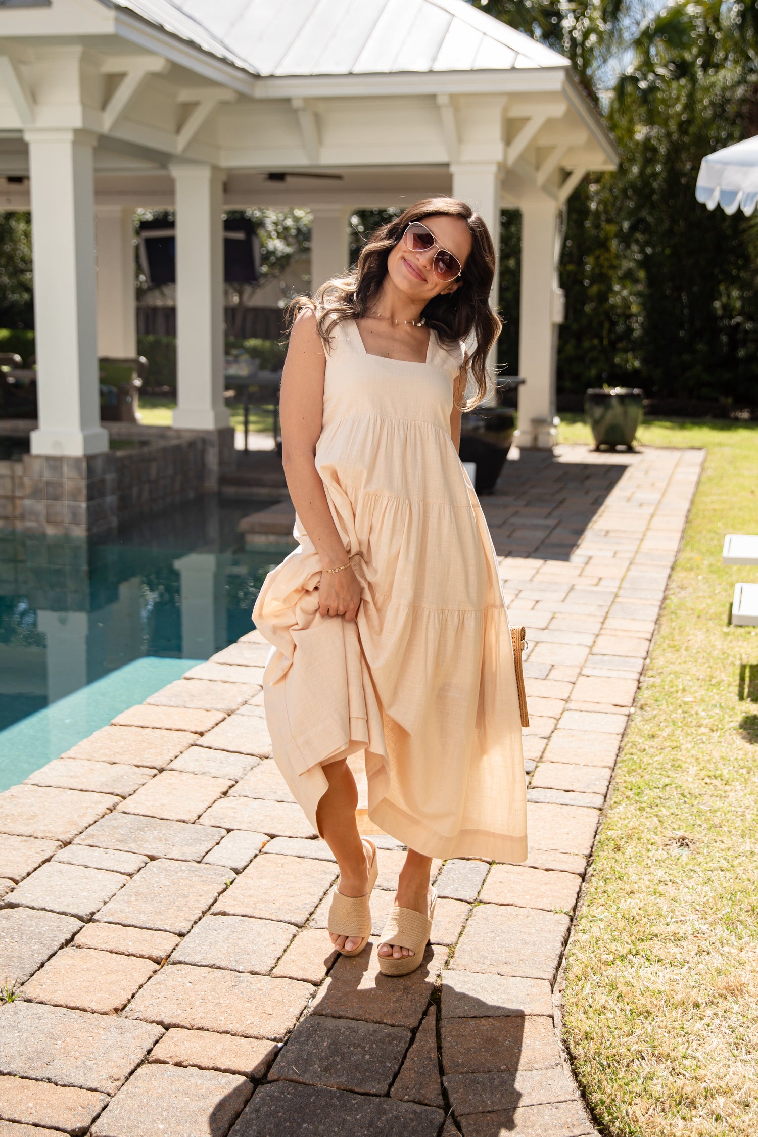 Woman in a beige dress standing by a poolside gazebo