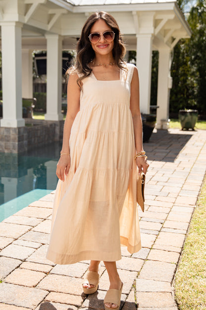 Woman in a beige dress standing by a poolside gazebo.