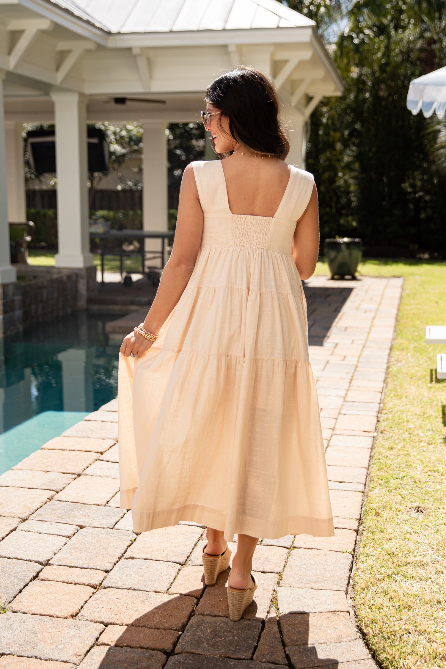 Woman in a beige dress walking by a poolside gazebo.