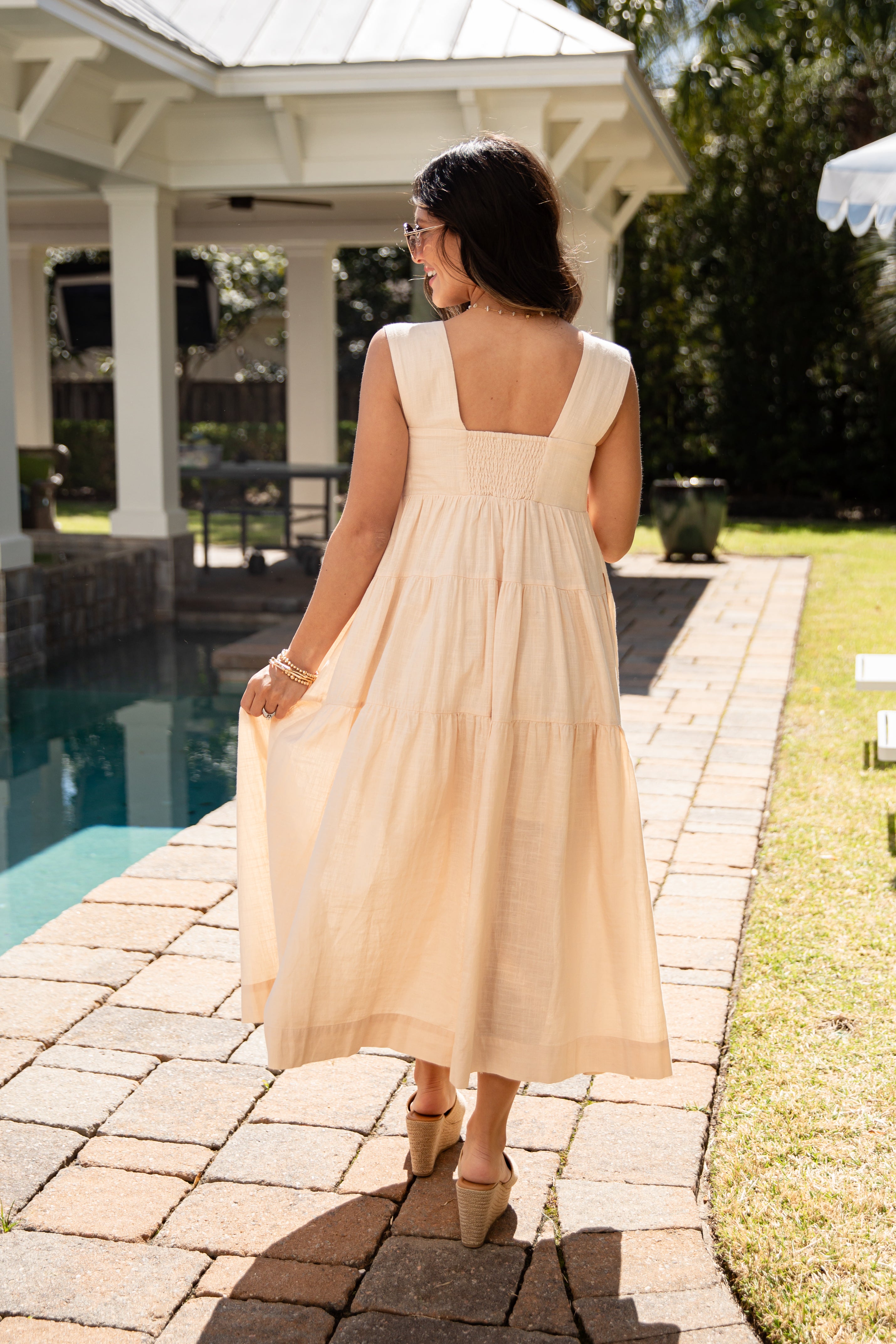 Woman in a beige dress walking by a poolside gazebo.
