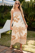 Woman in a floral dress standing outdoors with palm trees and a lounge chair in the background.