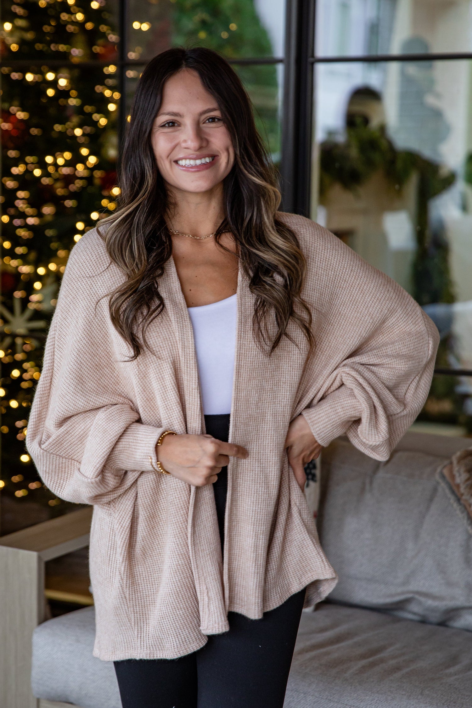 Woman wearing a beige cardigan in a cozy living room with Christmas decorations.