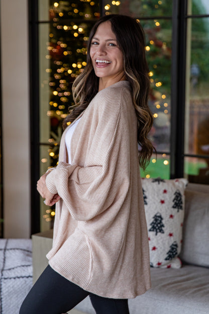 Woman wearing a beige cardigan in a cozy living room with Christmas decorations.