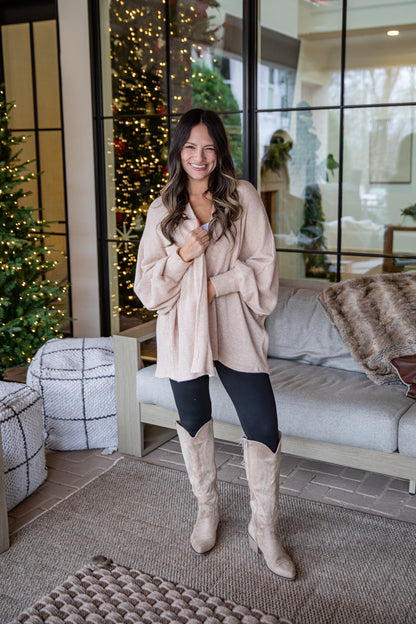 Woman in a beige coat and knee-high boots standing in a living room with Christmas decorations.