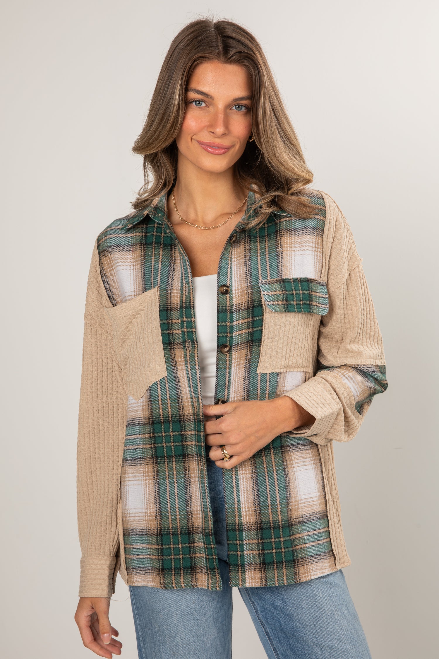 Woman wearing a plaid shirt over a beige sweater with a neutral background