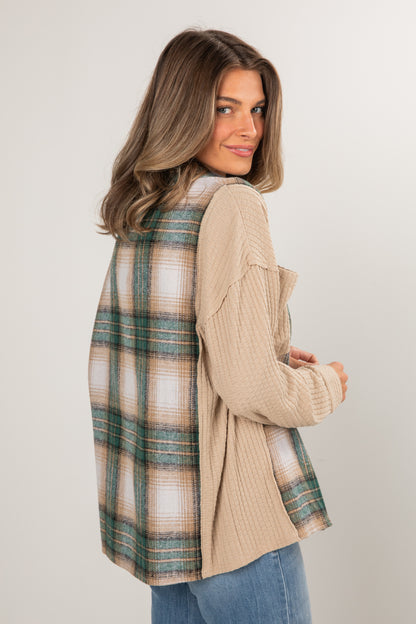 Woman wearing a beige cardigan over a plaid shirt on a plain background