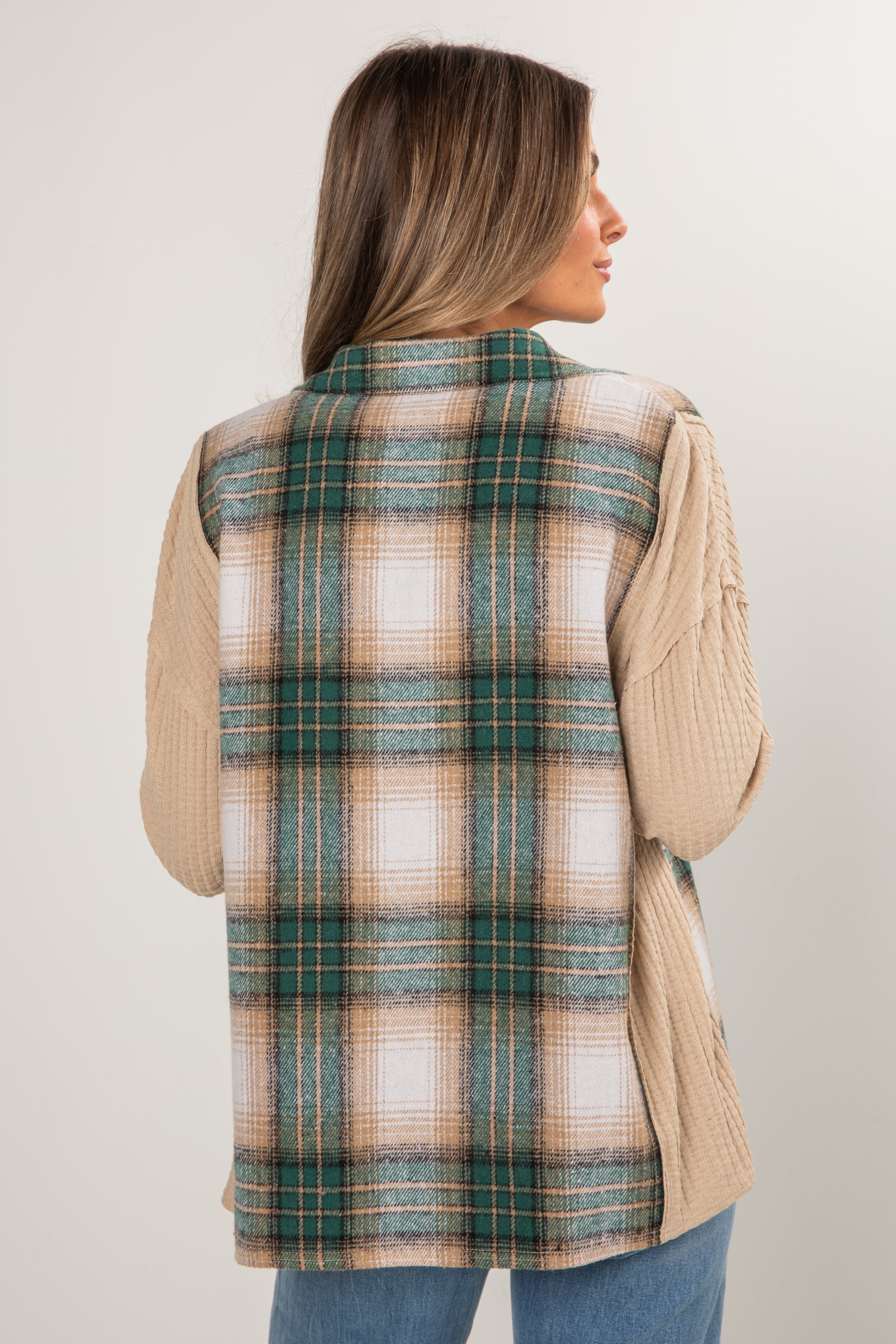 Woman wearing a plaid vest over a beige sweater on a plain background