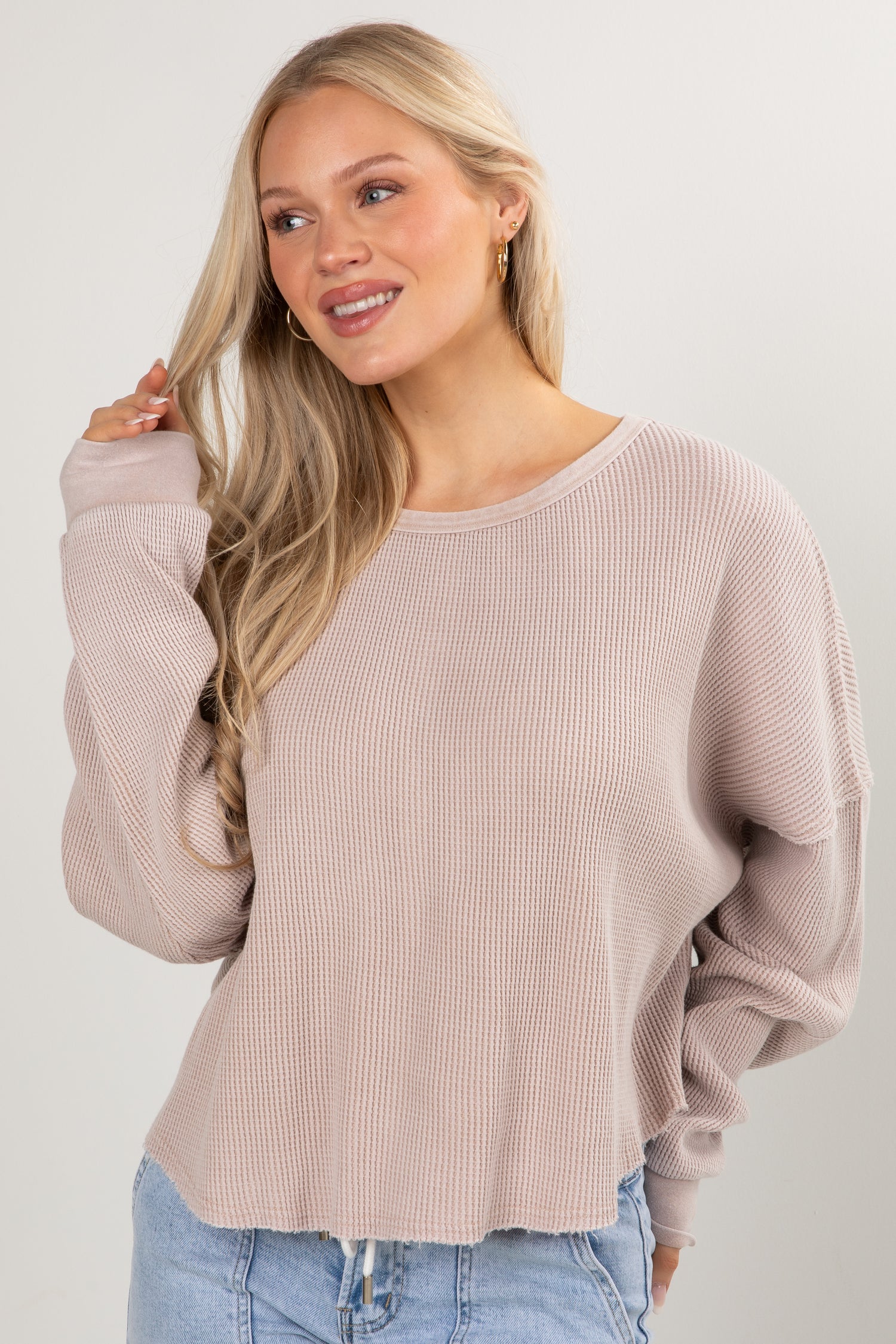 Woman wearing a beige sweater and blue jeans against a plain background