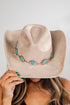 Beige cowboy hat with turquoise and silver decorative band held by a person against a neutral background