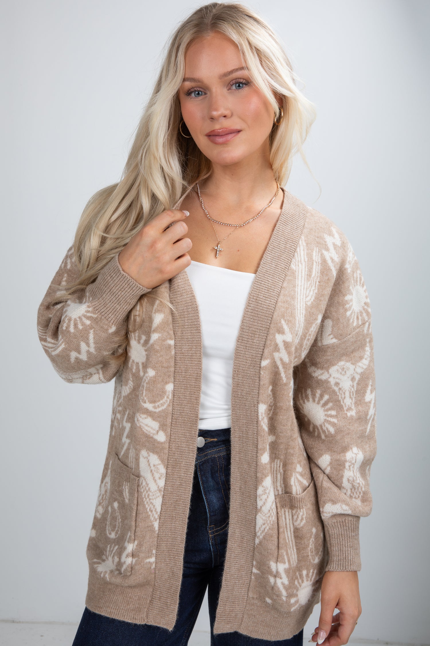 Woman wearing a beige patterned cardigan over a white top and jeans on a plain background
