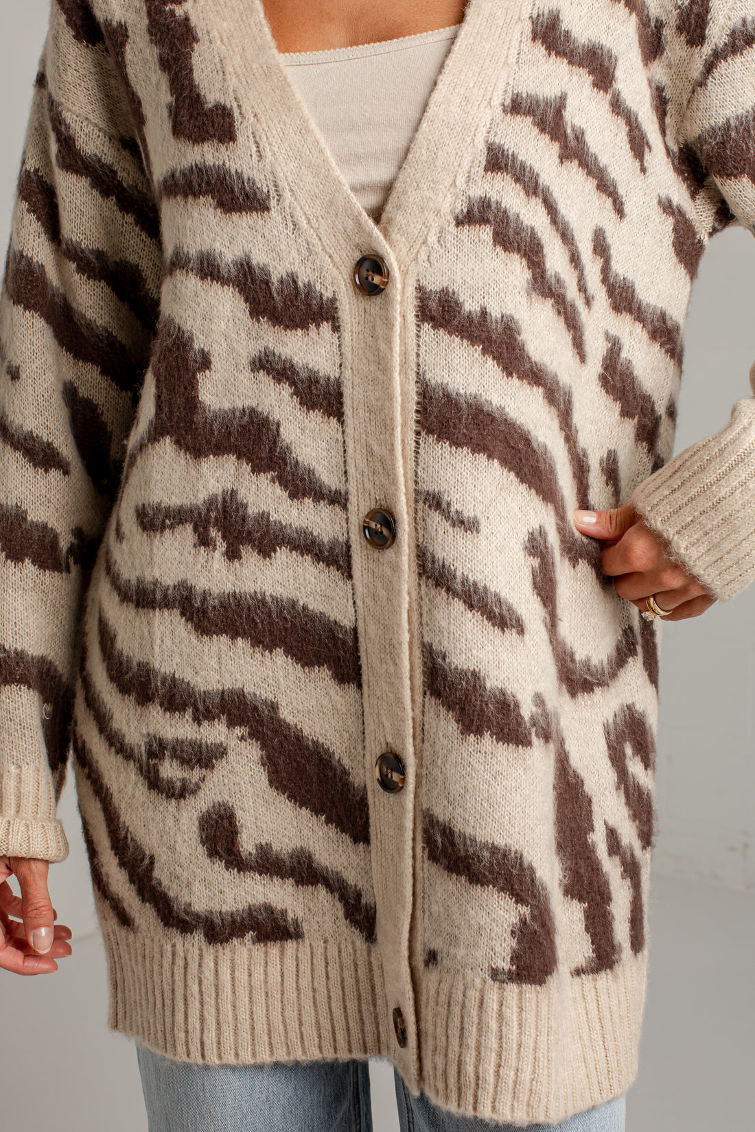 A close-up of a person wearing a chunky knit cardigan with a brown and cream zebra-like pattern, featuring dark buttons down the front.